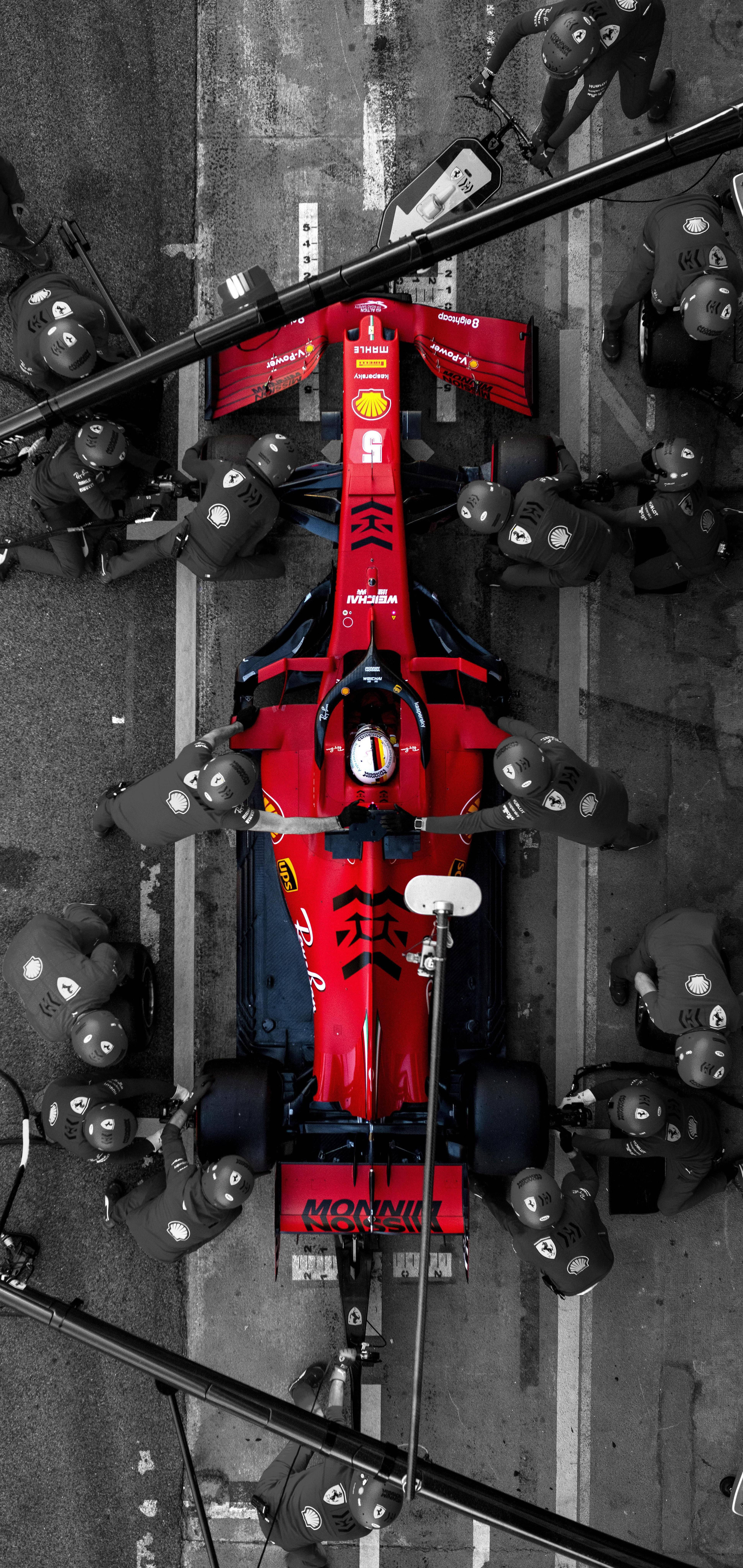 F1 法拉利車隊進站維修 iPhone 壁紙 — 賽道上維修站中，一輛紅色一級方程式賽車被機械師包圍的鳥瞰圖。