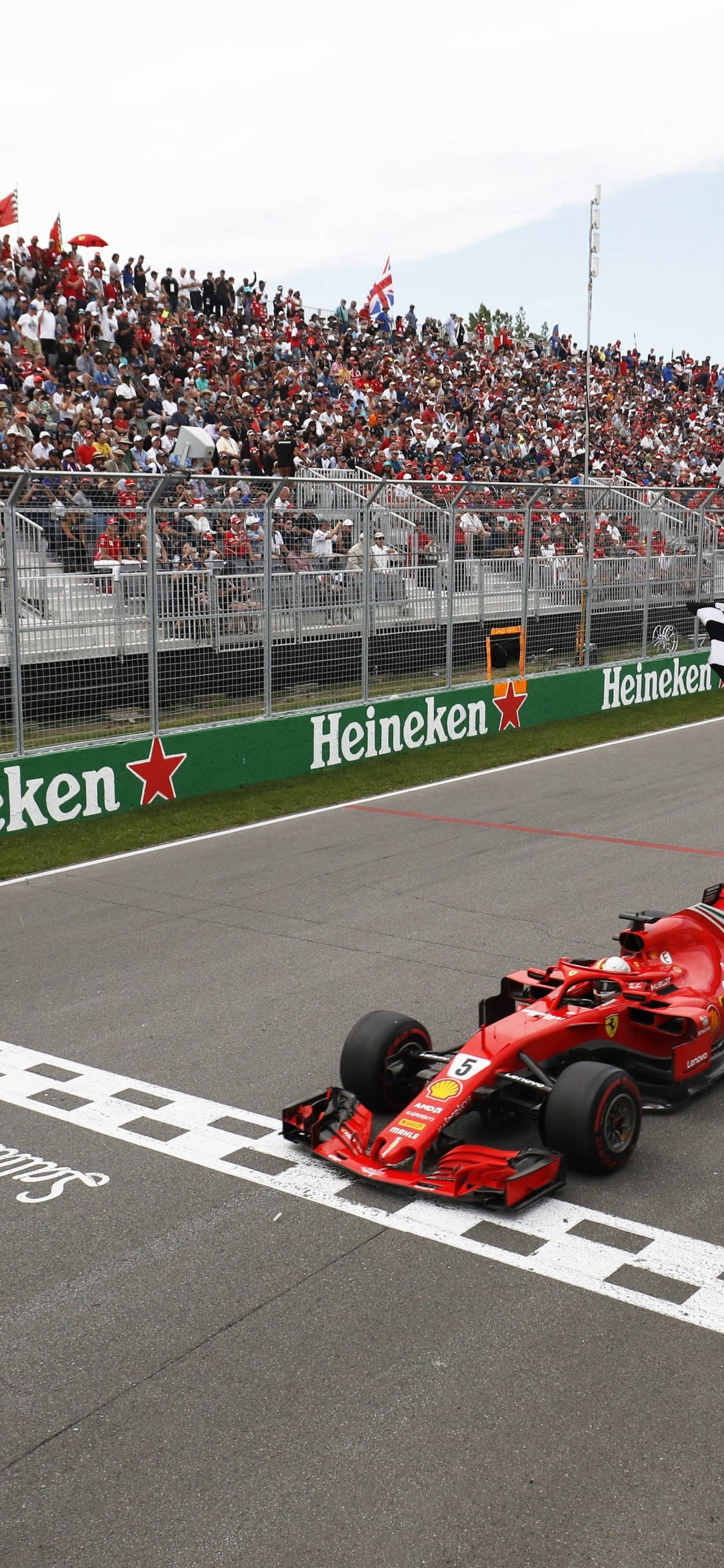 F1 賽車維特爾 過線 iPhone 壁紙 — 一輛紅色一級方程式賽車越過格仔旗終點線，安全屏障後的看台上擠滿了歡呼的車迷。