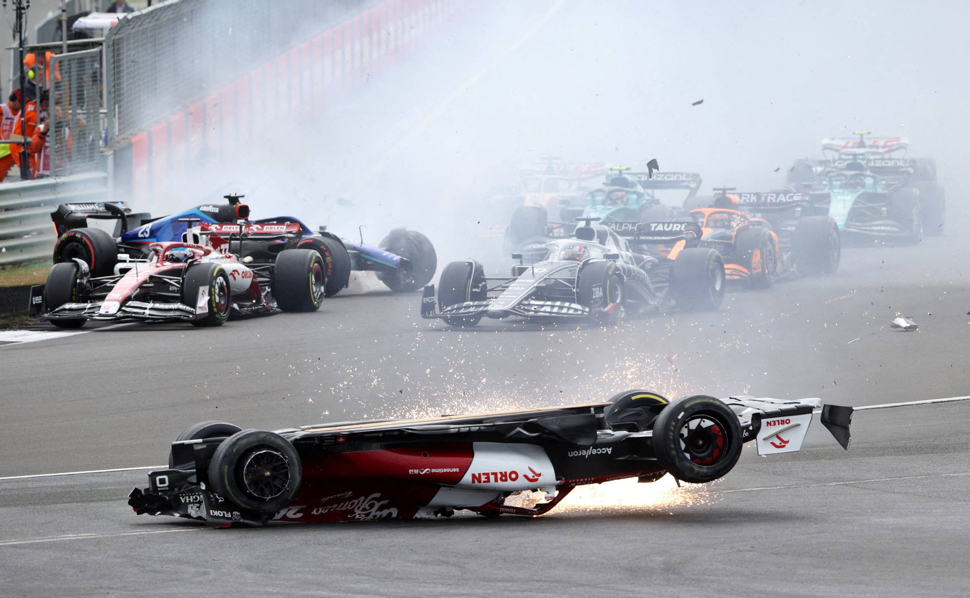 F1 賽車賽道上驚心動魄的撞車事故 壁紙 — 一級方程式賽車在賽道上翻轉，多車相撞冒出濃煙和火花。