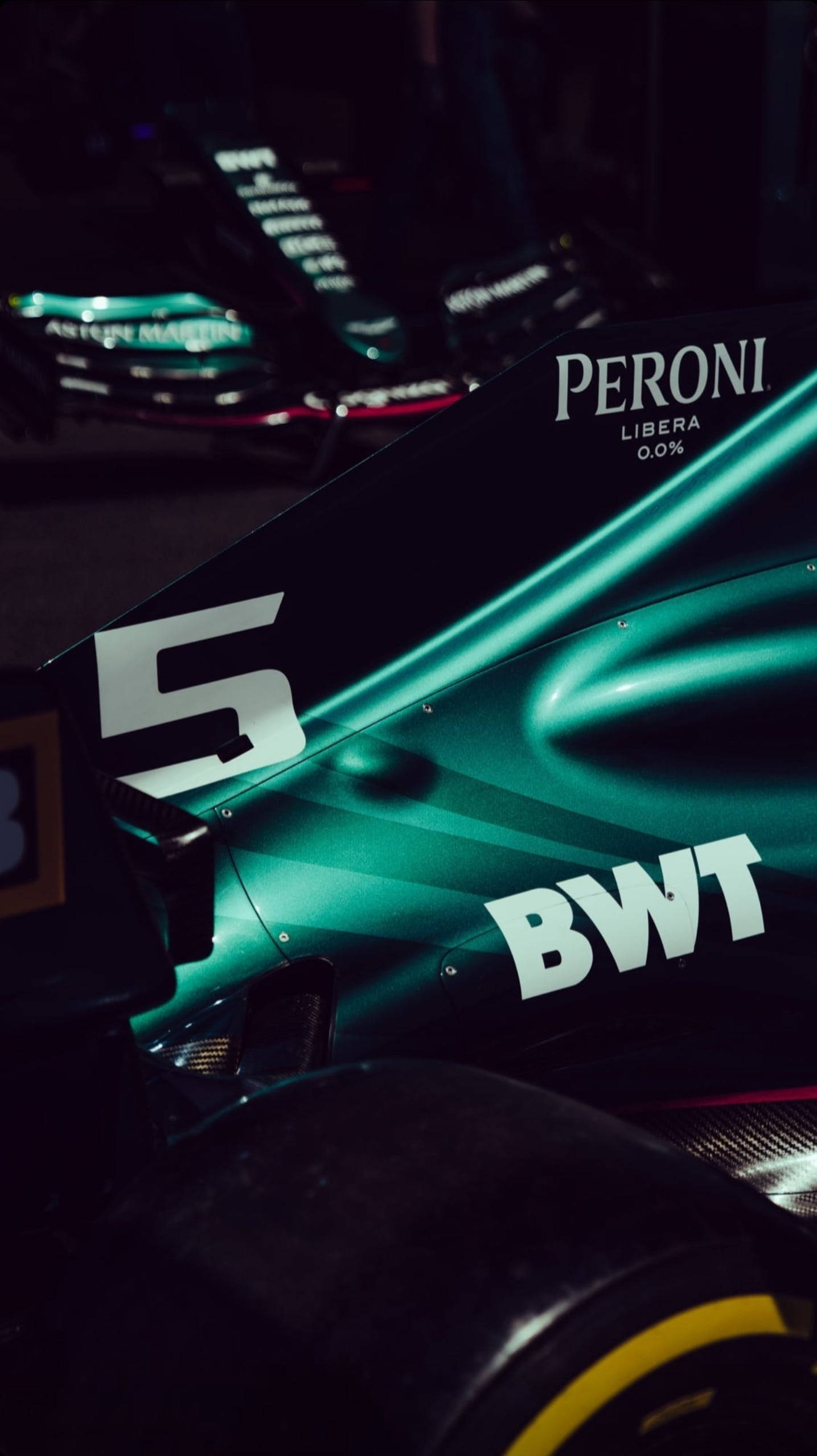 F1 阿斯頓·馬丁 cognizant iPhone 壁紙 — 近距離拍攝時尚綠色賽車的後翼和輪胎，在戲劇性燈光下帶有贊助商標誌。