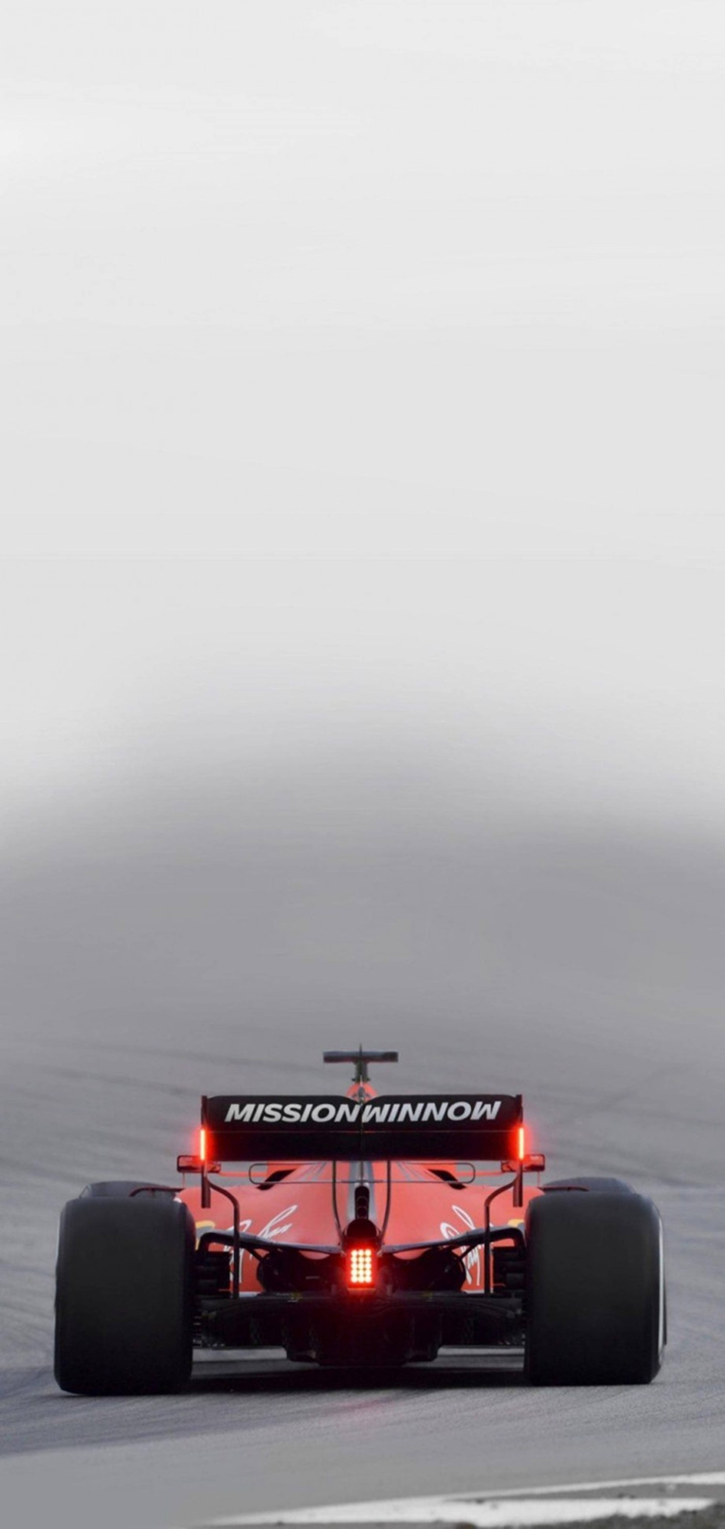 F1手機2022紅法拉利 壁紙 — 一輛帶有「MISSION WINNOW」標誌的紅色一級方程式賽車在霧濛濛的賽道上疾馳而去，尾燈閃爍明亮。
