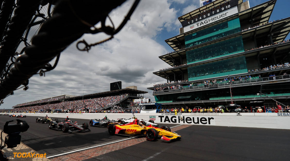 F1賽車在印第安納波利斯500賽事中的驚險速度 壁紙 — 印第安納波利斯賽車場上，IndyCar 賽車在陰天之下飛馳而過滿座看台的壯觀景象。