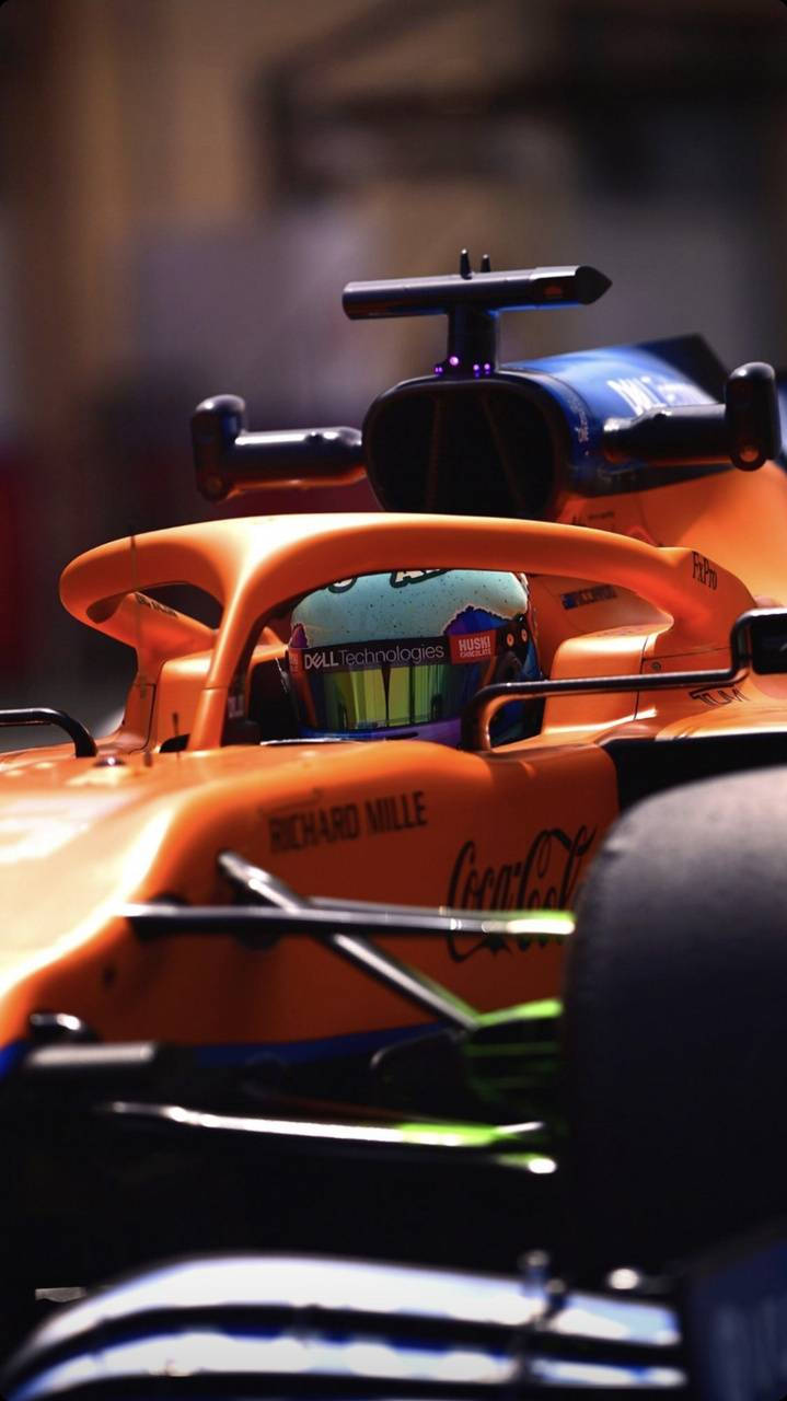 F1車手丹尼爾·里卡多賽車內的精彩近照 壁紙 — 橙色一級方程式賽車特寫，車手戴頭盔在駕駛艙內，處於明亮燈光下。