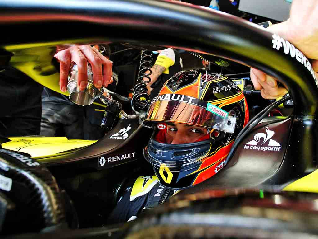 F1車手埃斯特班·奧康全速競賽 壁紙 — 一名戴著雷諾頭盔的F1車手在駕駛艙內從維修站工作人員手中接過飲料。