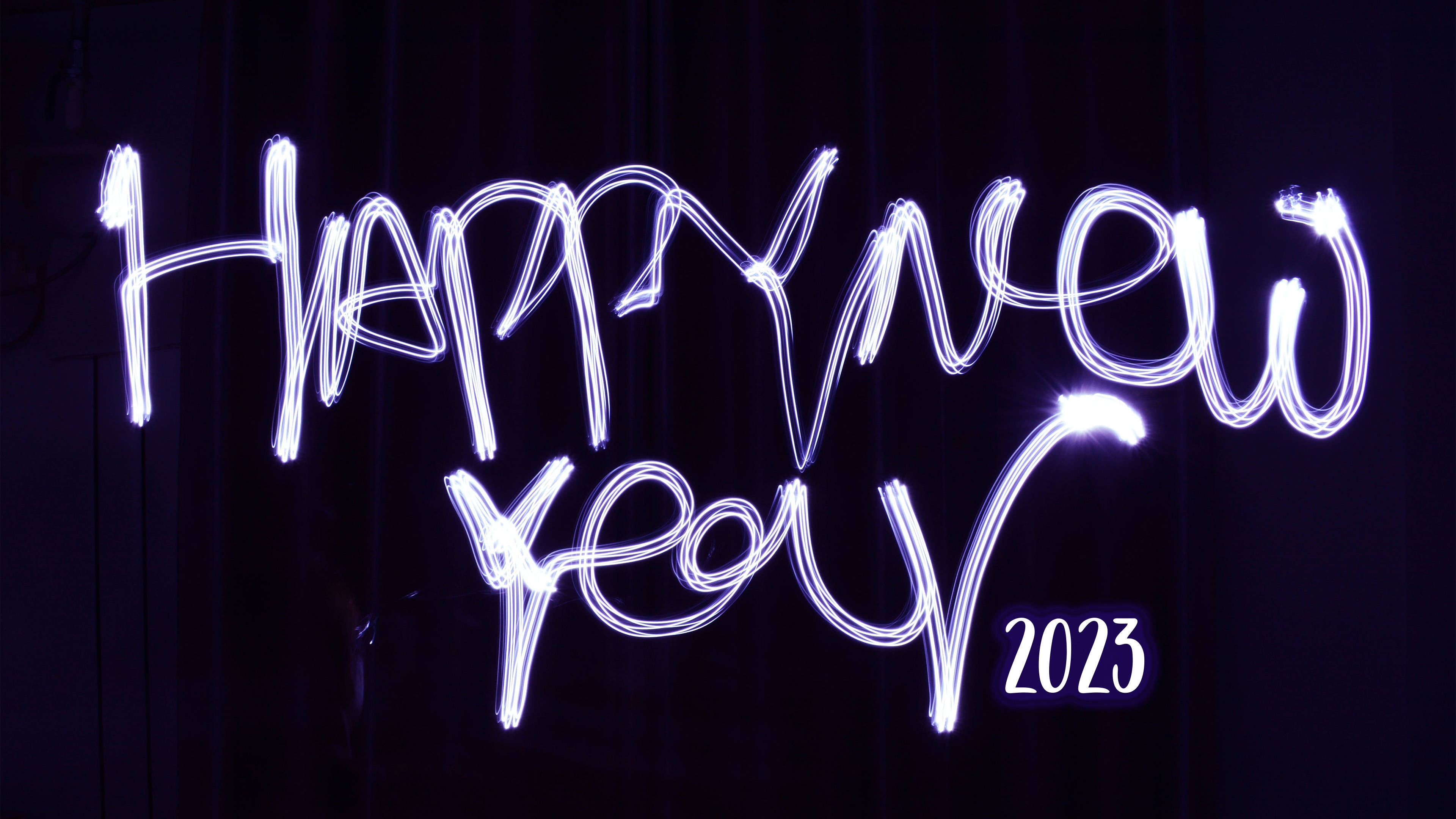 在深色背景下，用發光的白色光跡寫成的 Happy New Year 2023。