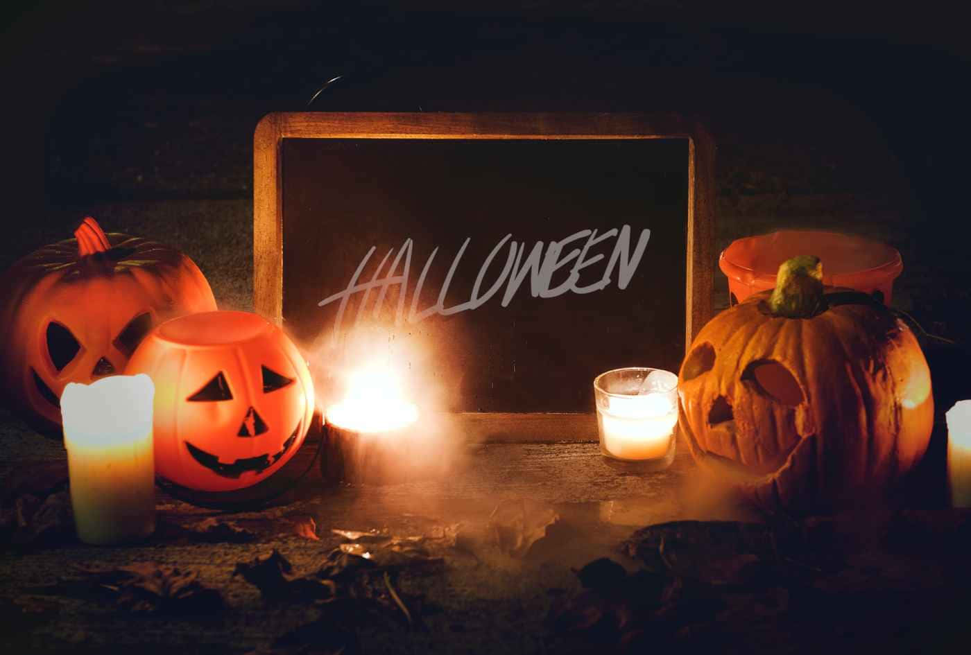 壁紙 — 發光的傑克南瓜燈和閃爍的蠟燭在寫著Halloween的黑板上投射出詭異的光芒，周圍環繞著秋葉。