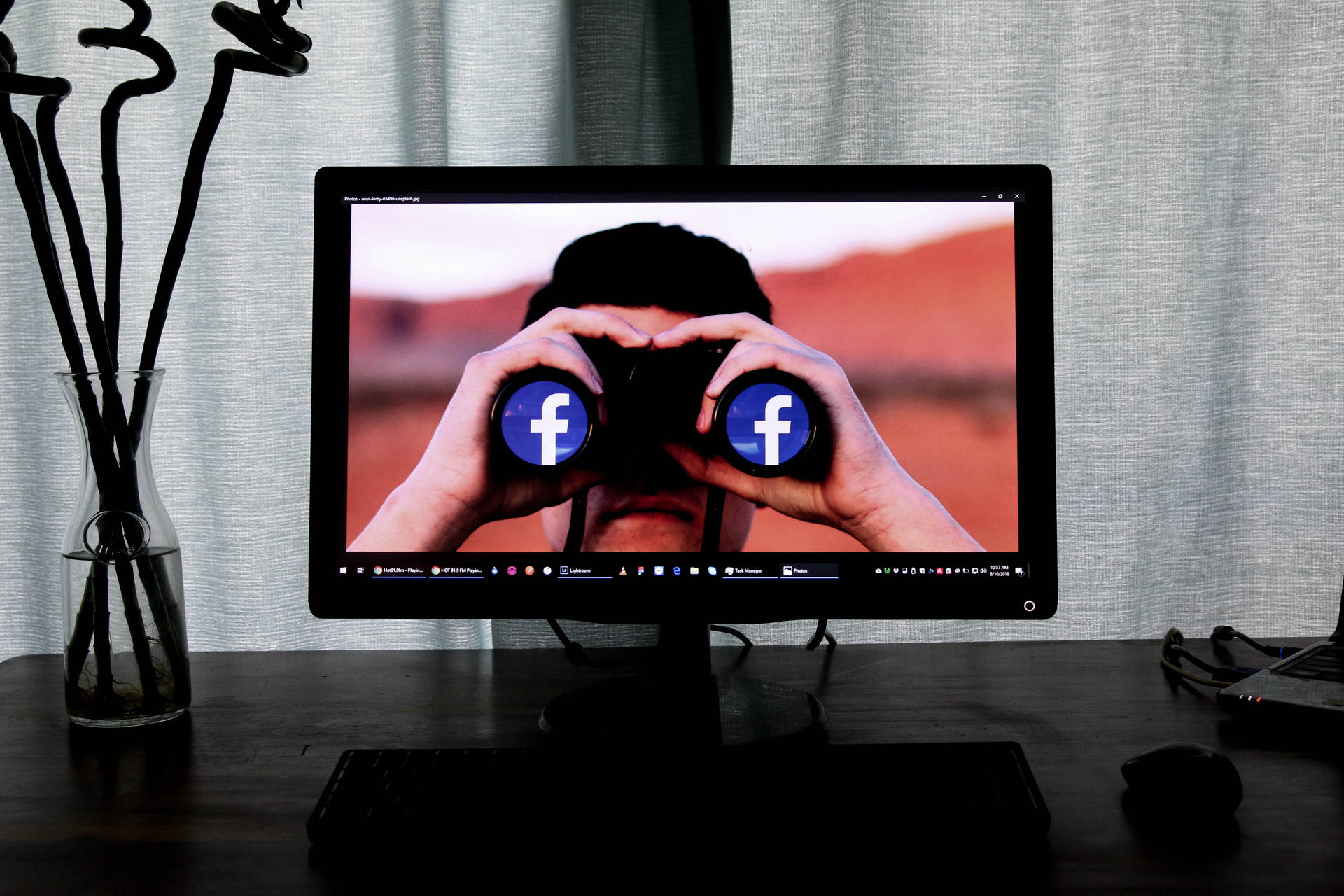 電腦顯示器顯示一個人使用雙筒望遠鏡，鏡片上有Facebook標誌，背景是沙漠。