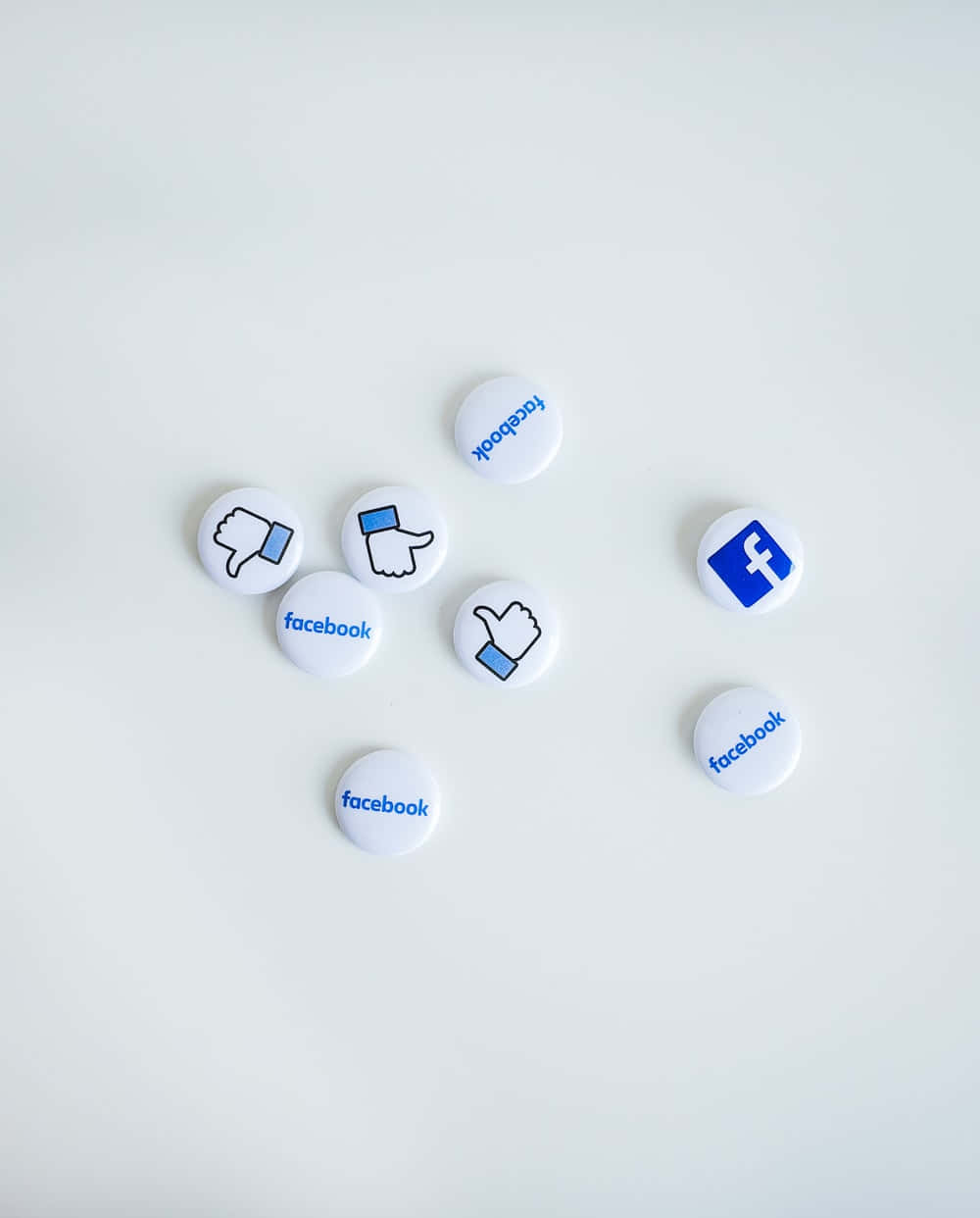 散落的Facebook按鈕，帶有讚/不讚圖標和標誌，在淺灰色背景上。