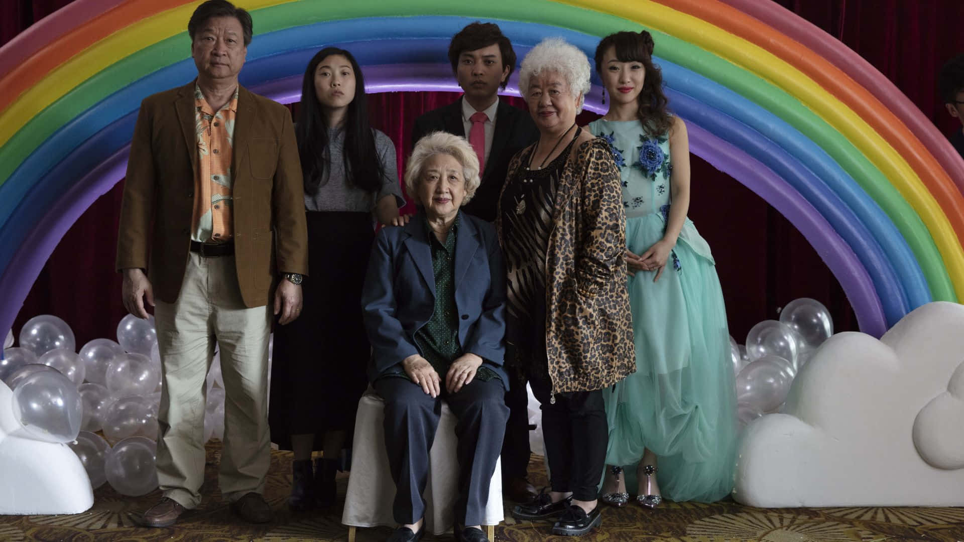 The Farewell 桌布 壁紙 — 一個六人家庭在一個大型充氣彩虹拱門和白色雲朵裝飾及銀色氣球前正式擺姿勢。