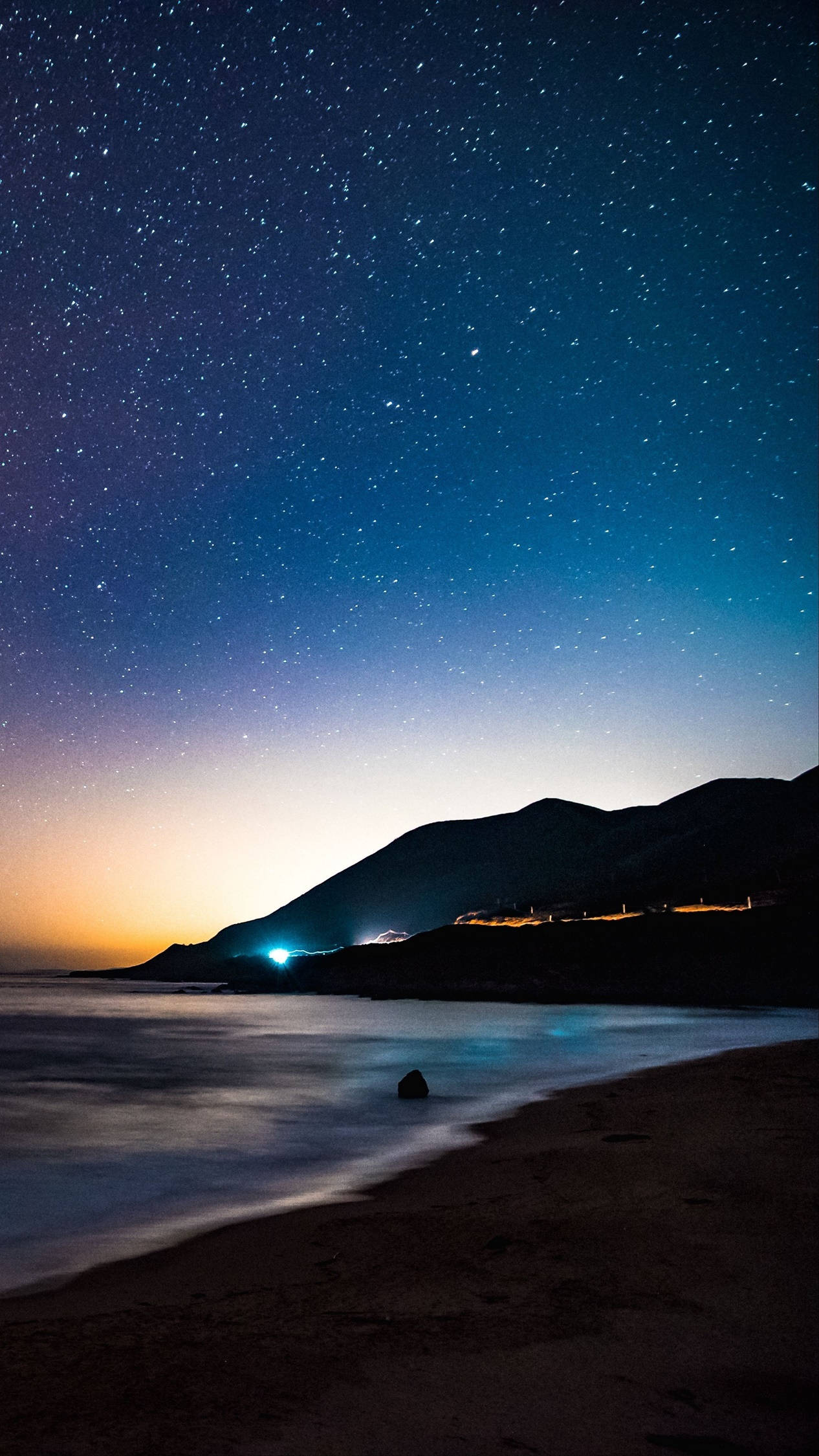 繁星點點的夜晚，海灘上有山丘和沿岸的遠方燈光。