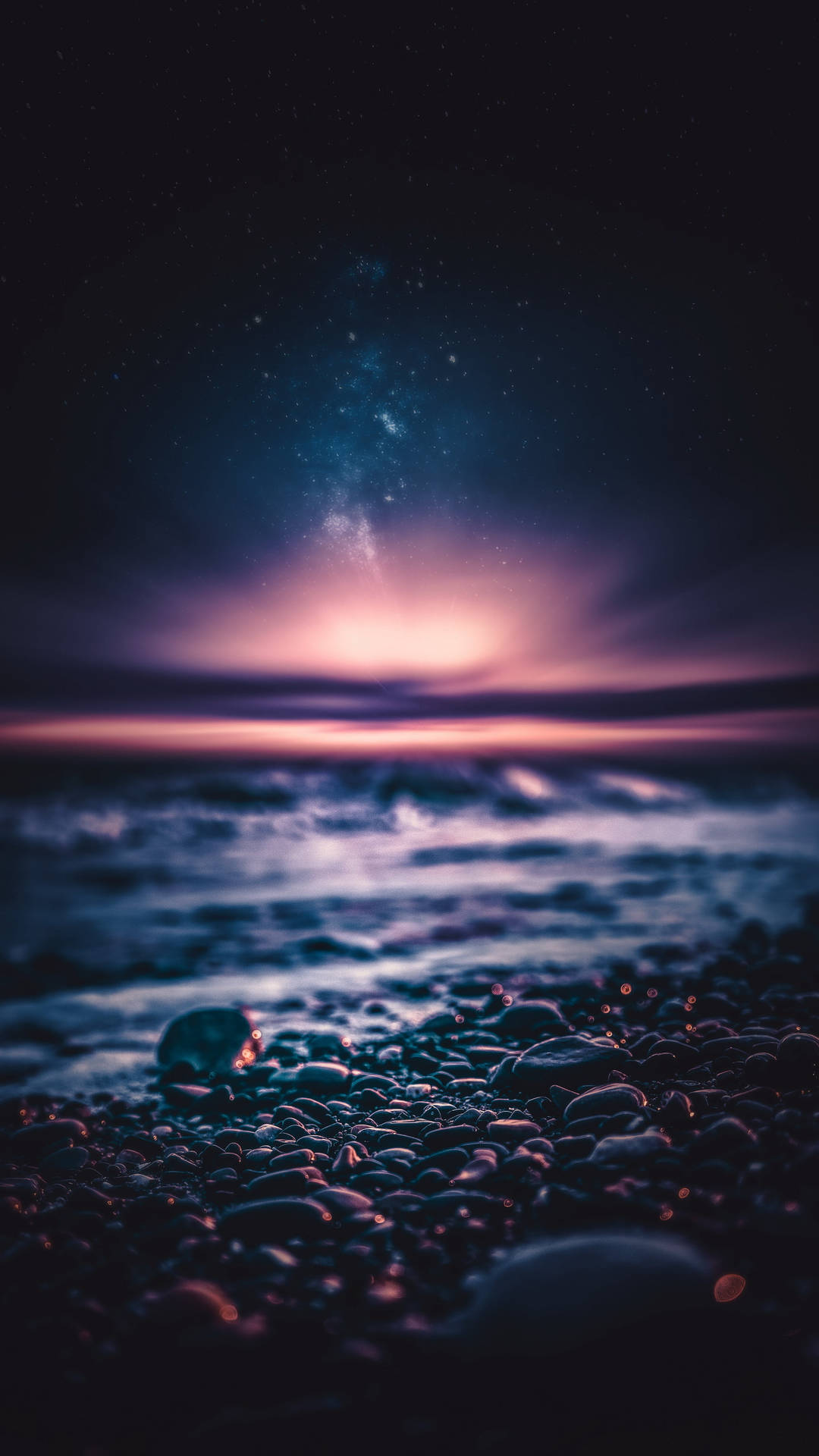 繁星點點的夜空下，鵝卵石海灘與溫柔的海浪。
