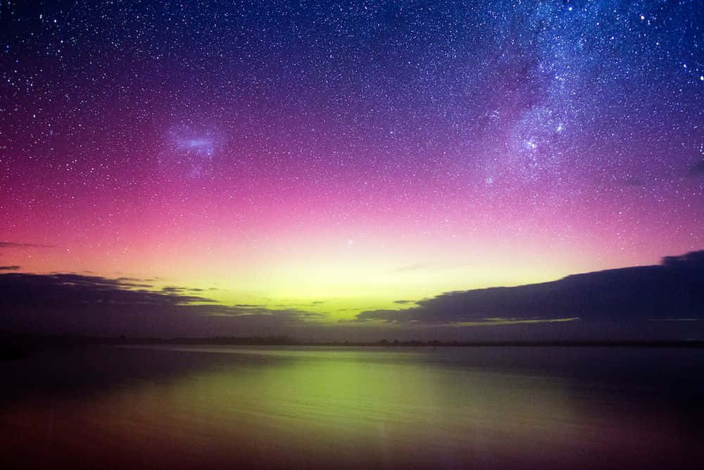  壁紙 — 繁星點點的紫色和粉紅色夜空，銀河在平靜的反射湖面上拱起，下方是發光的雲朵。