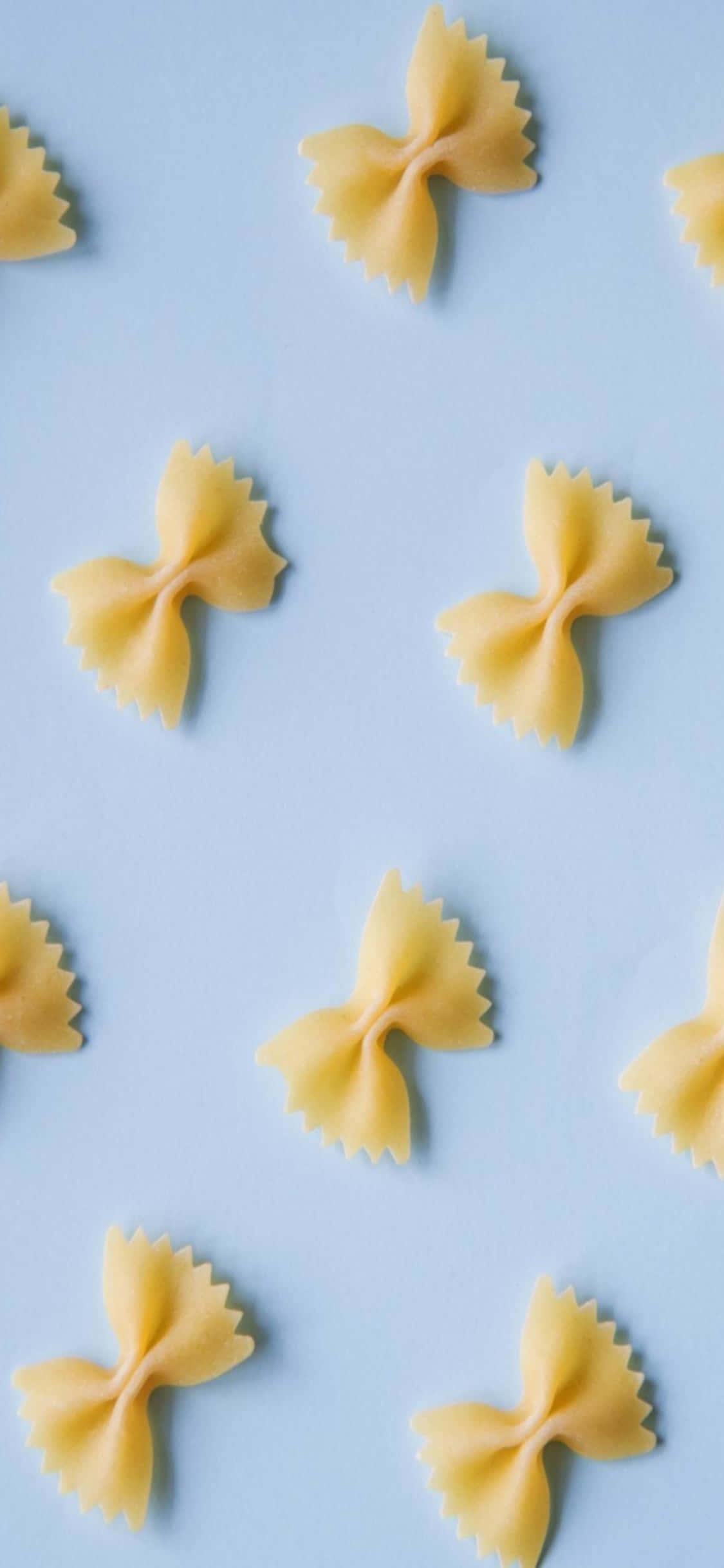 Farfalle iPhone X 義大利麵背景 壁紙 — 蝴蝶結意粉散落在柔和的藍色背景上，形成極簡的平鋪構圖。