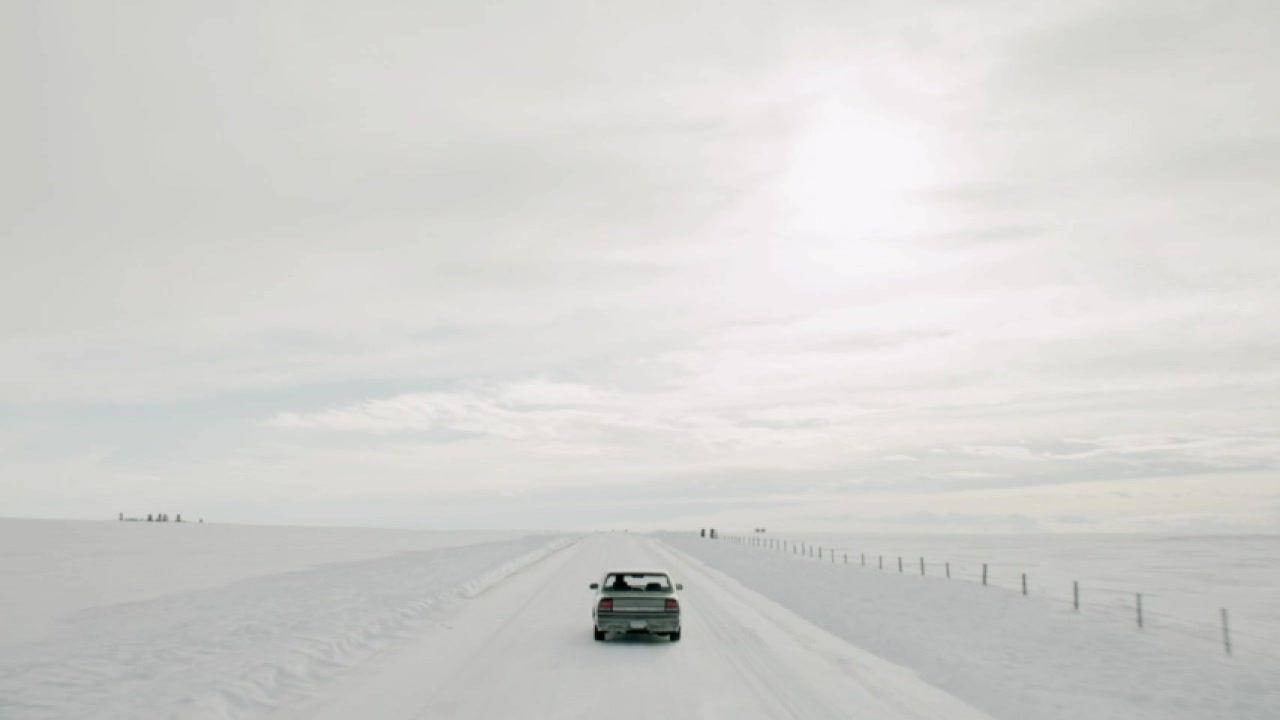 銀色小型貨車在雪路上行駛，穿越冰凍的沙漠景觀。