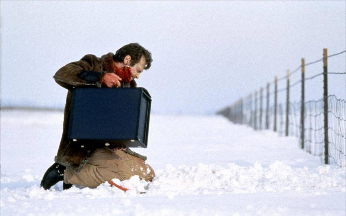 男子跪在雪中，籬笆旁手持黑色盒子