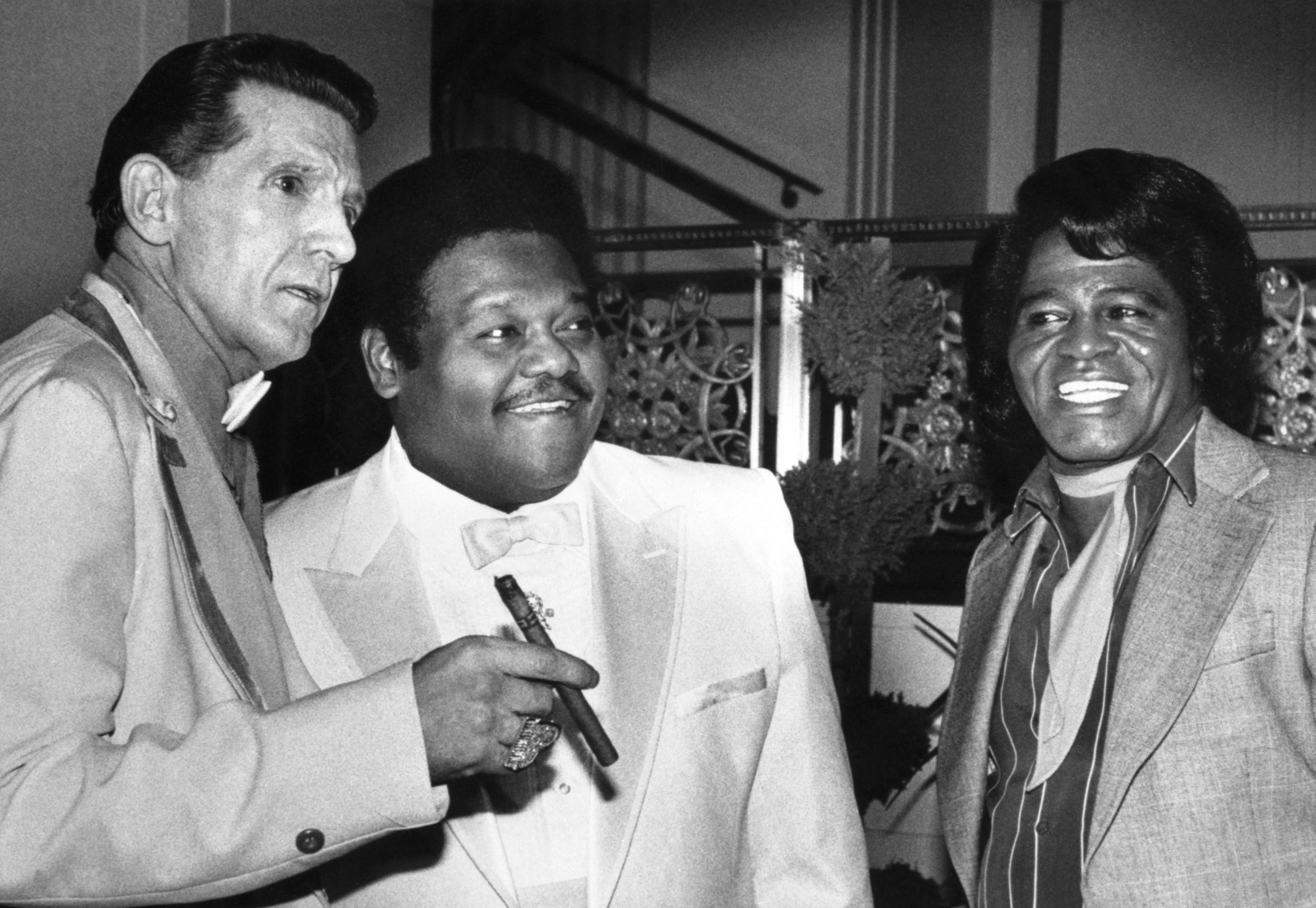 Fats Domino、Jerry Lee Lewis 與 Little Richard 壁紙 — 三位時尚男士身著正裝，在裝飾華麗、燈光溫暖的優雅室內活動中一起擺姿勢。