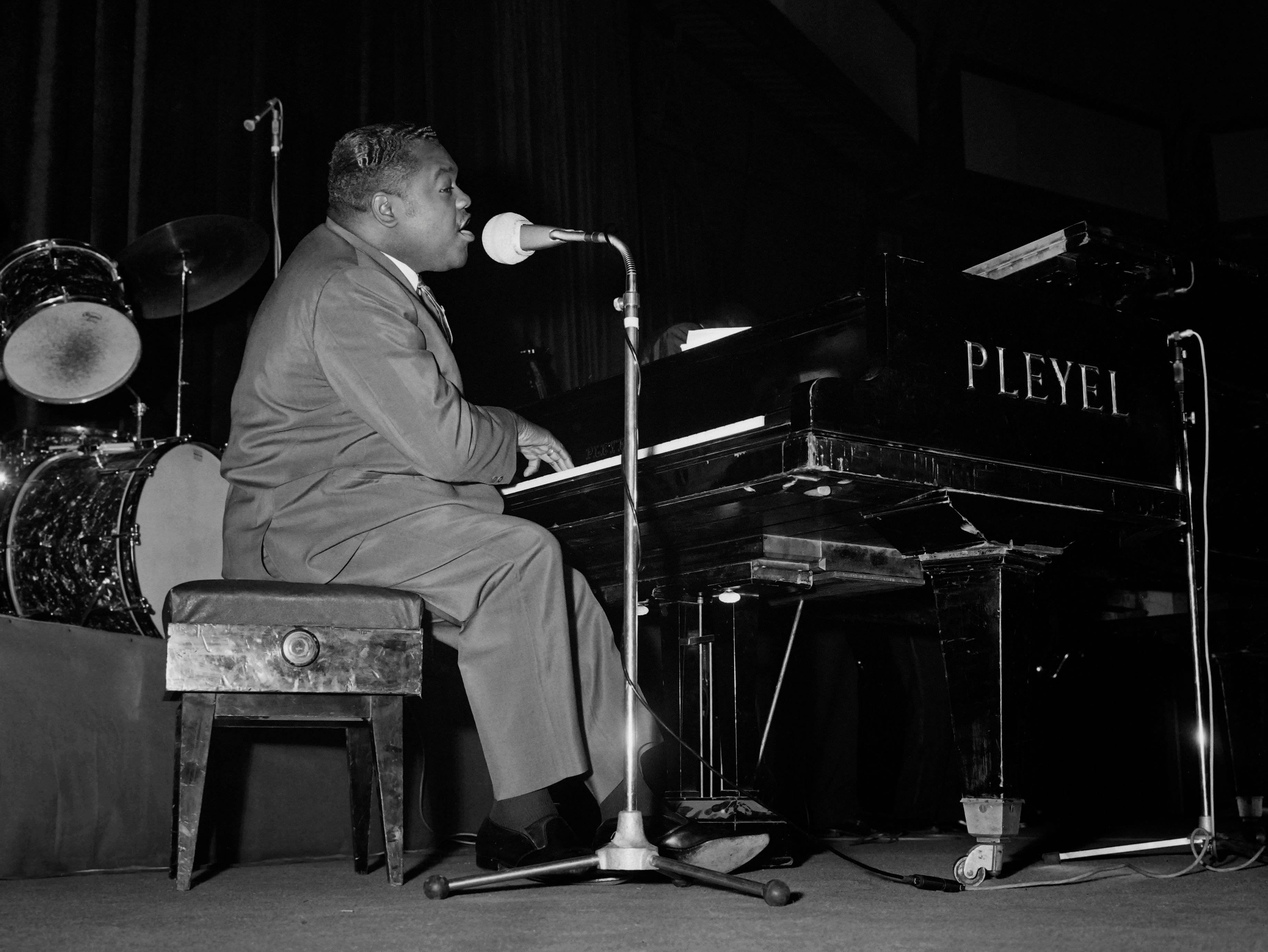 Fats Domino 歌手鋼琴家 壁紙 — 一位身穿西裝的爵士鋼琴家在舞台燈光下熱情地彈奏Pleyel三角鋼琴，身後有爵士鼓。