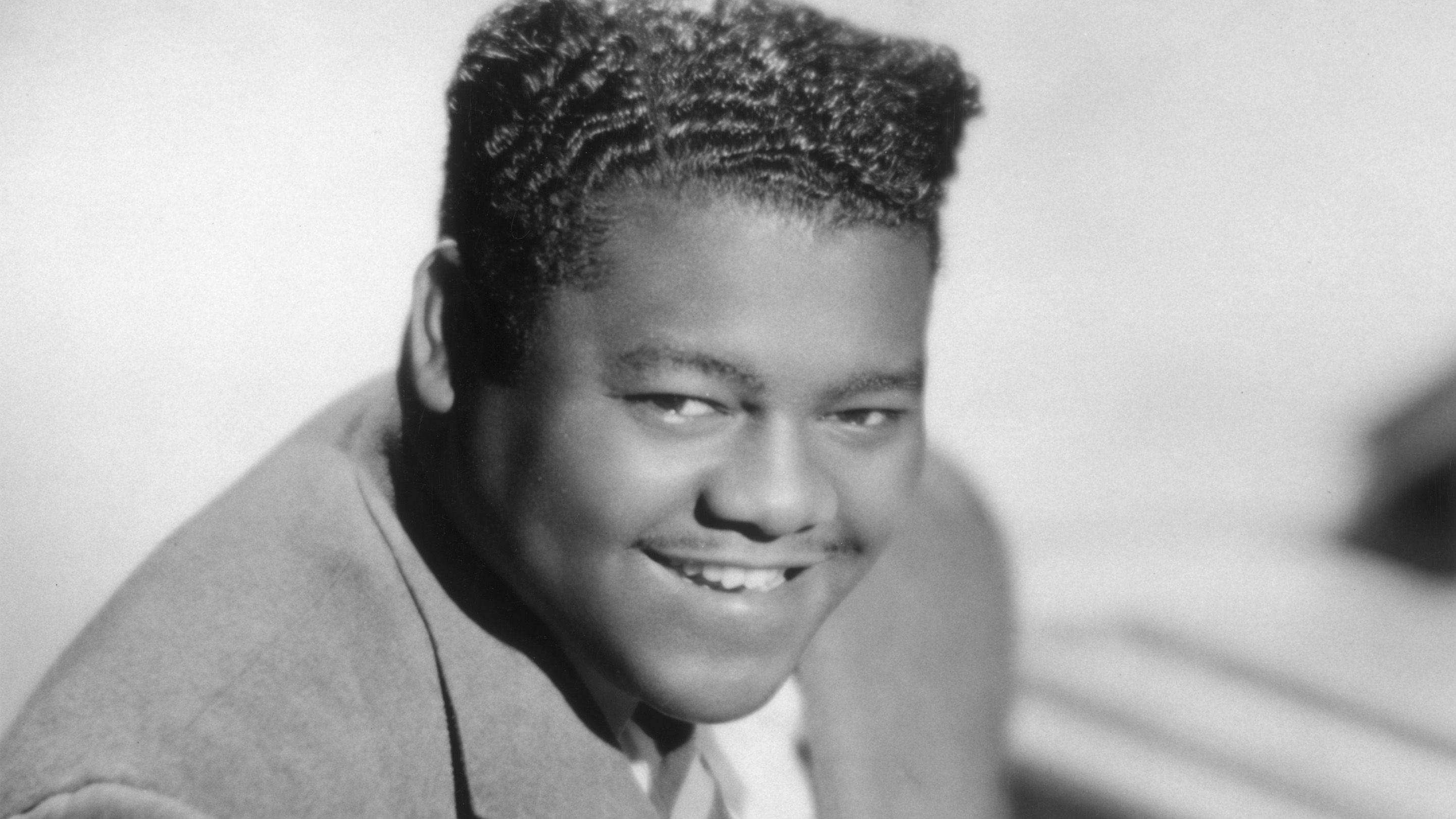 Fats Domino 黑白舊照 壁紙 — 一位微笑的黑人男士，梳著時尚髮型，身穿西裝外套，在經典的黑白肖像中擺姿勢。