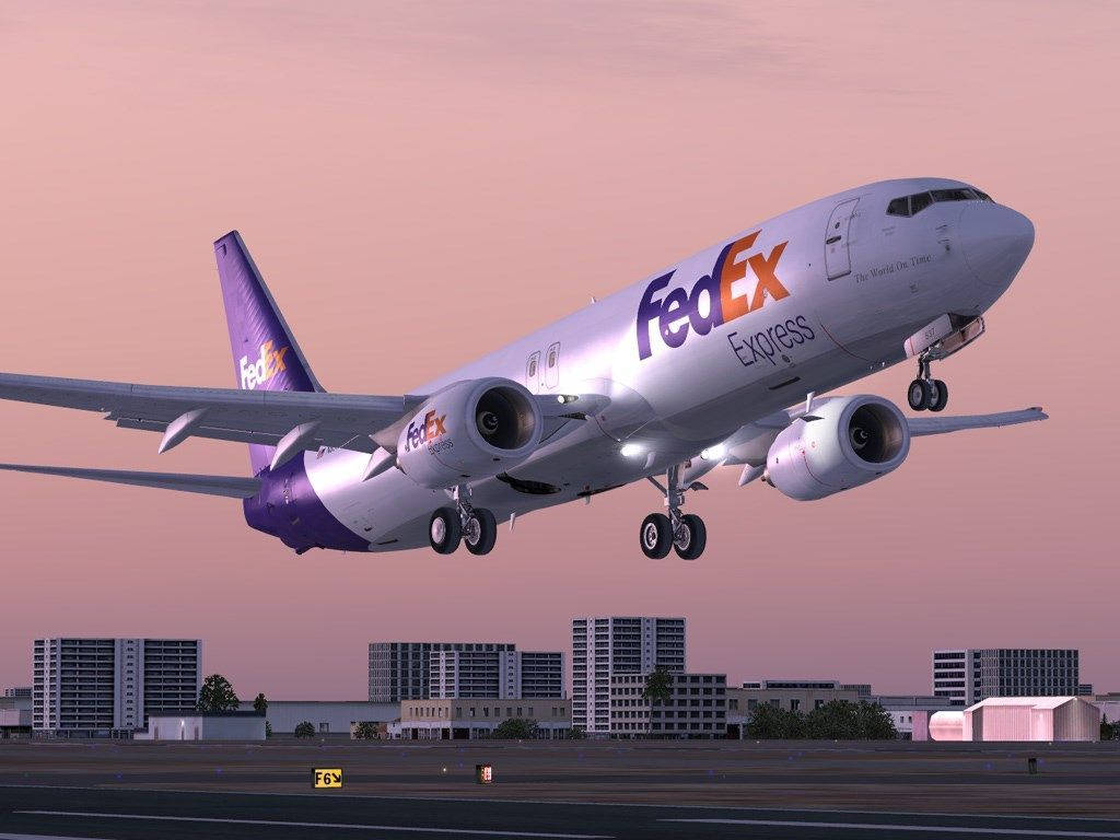FedEx Express數位攝影 壁紙 — 一架聯邦快遞貨運飛機在現代城市景觀上空，在柔和的粉紅色暮色天空中下降。