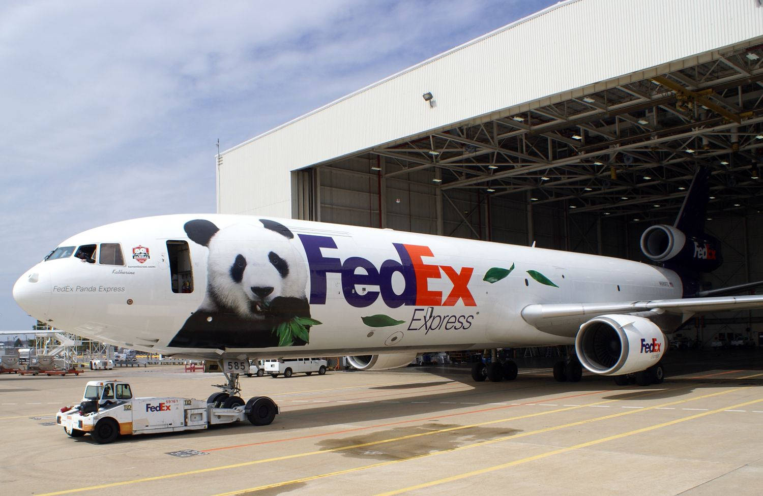 FedEx Panda Express 壁紙 — 一架帶有巨型熊貓設計的聯邦快遞快遞飛機停在機庫下的機場閘口。