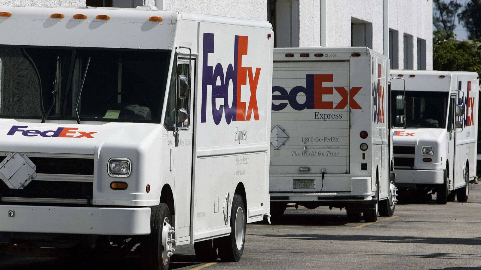 一排FedEx送貨車停在陽光明媚的城市停車場。