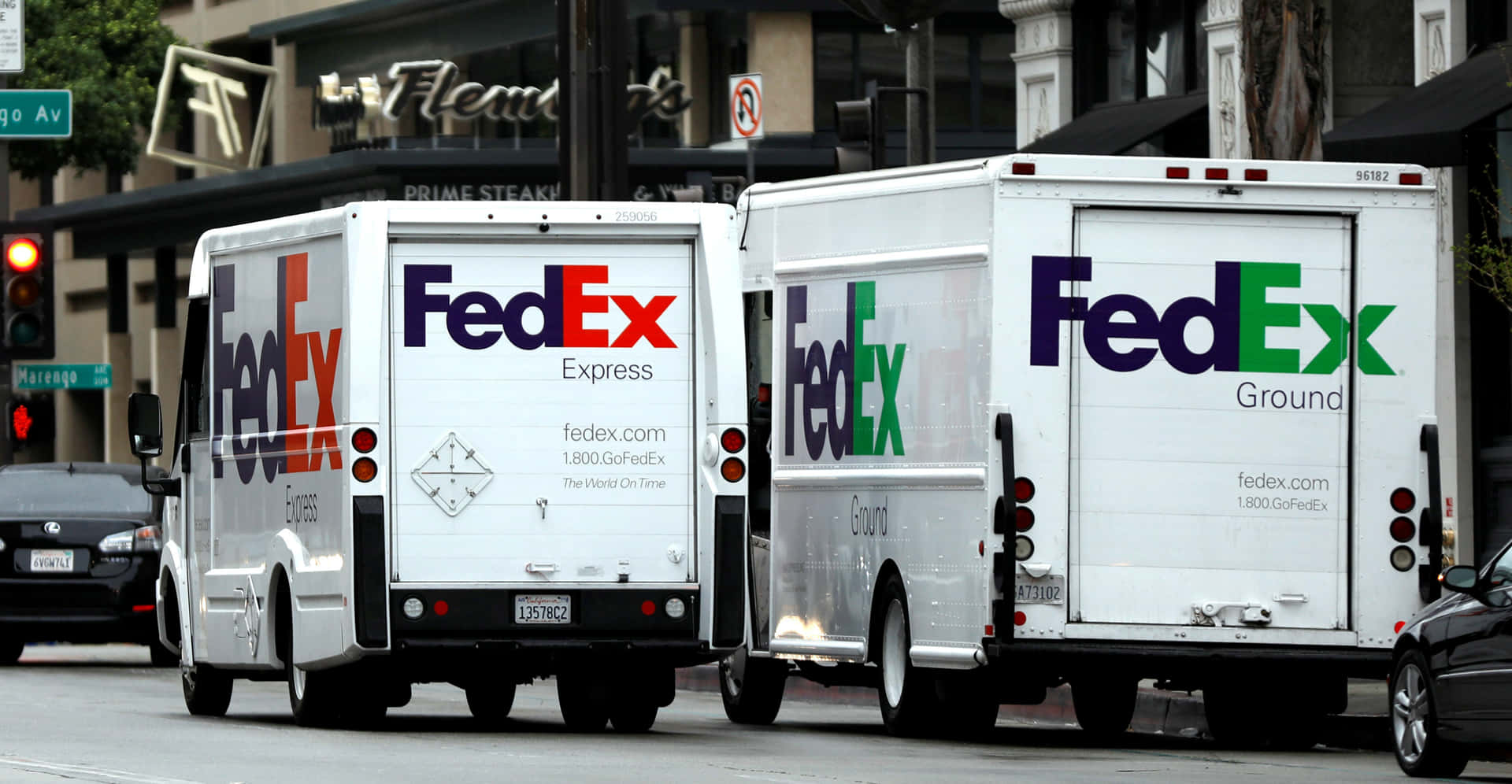 兩架FedEx送貨貨車停泊在城巿街道上，靠近商店門面。