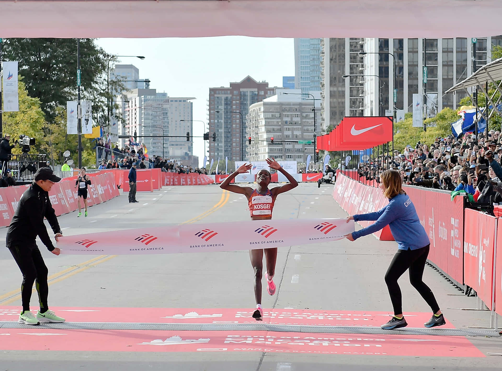  壁紙 — 一位女跑手高舉雙臂，以勝利姿態衝過城市馬拉松的終點線，群眾歡呼，工作人員拉著終點帶。
