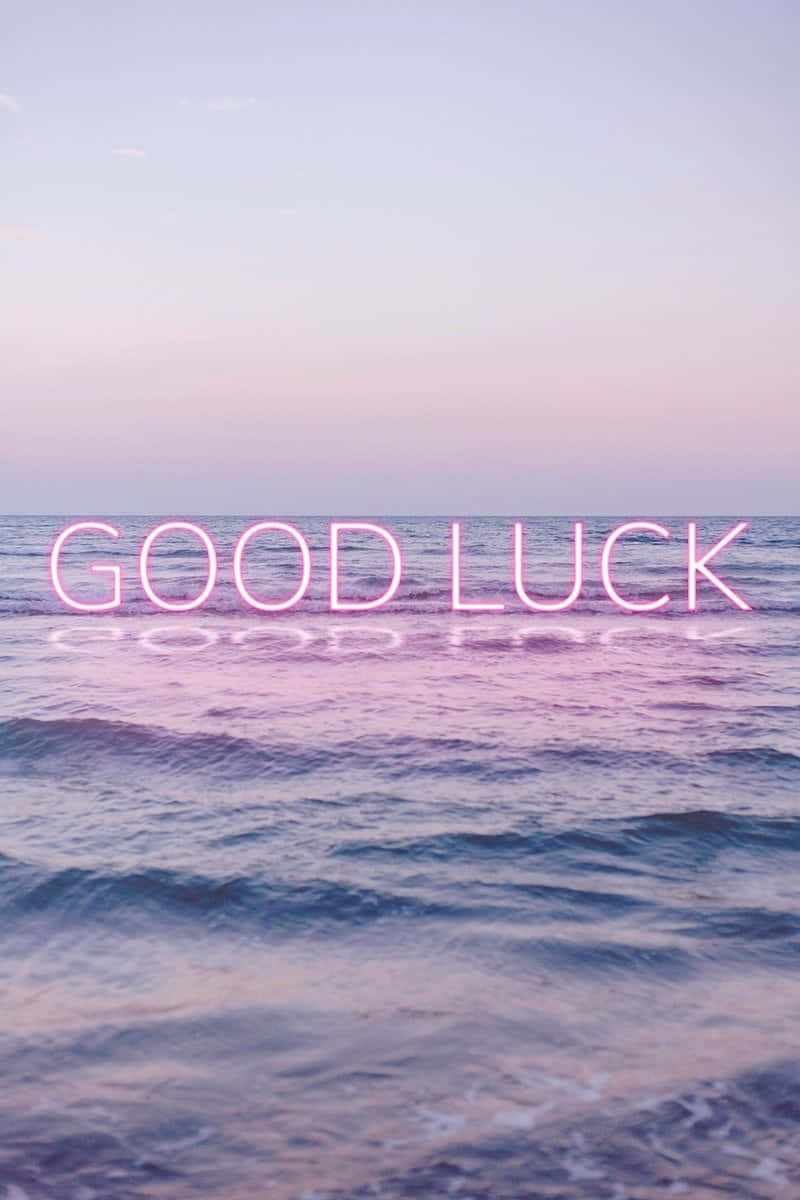  壁紙 — 粉紅色霓虹燈 'GOOD LUCK' 文字漂浮在黃昏平靜的海浪上，伴隨著柔和粉彩的天空。
