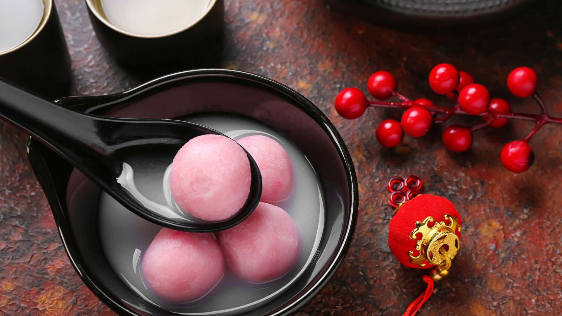  壁紙 — 粉紅色糯米糰在清湯中漂浮，放在黑色碗中，旁邊有紅色漿果和節日裝飾。