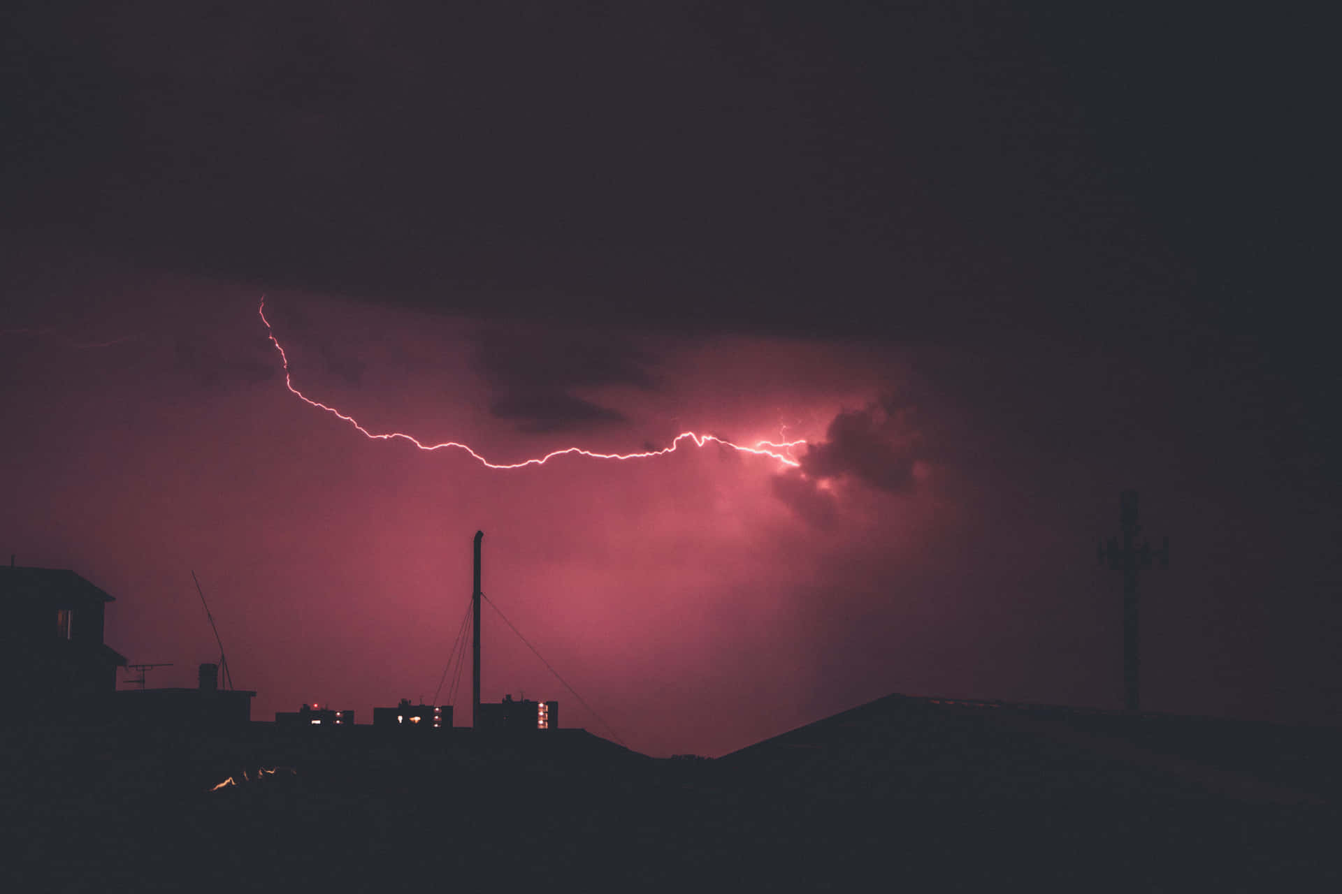 粉紅色閃電照亮了黑暗城市屋頂上方的暴風雨之夜。