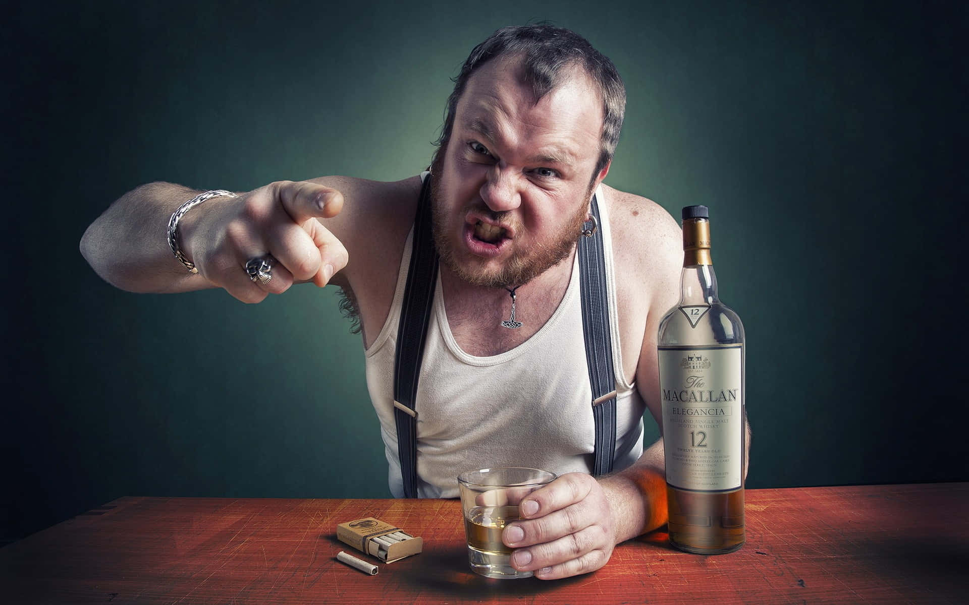  壁紙 — 一個穿著背心和吊帶褲的憤怒男人，一邊拿著一杯威士忌，旁邊放著一瓶The Macallan，一邊憤怒地指向鏡頭。