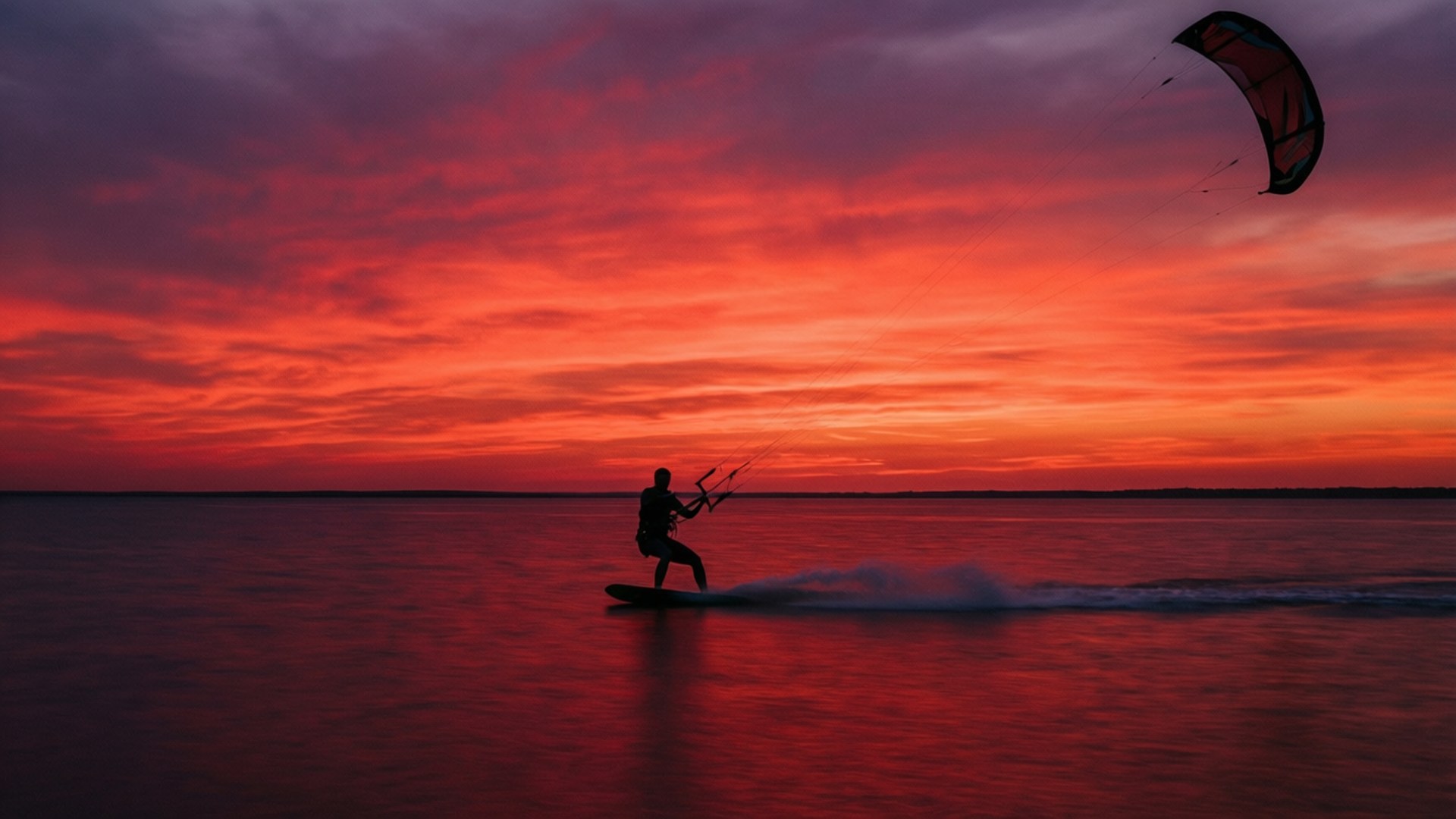 Kite Surf 桌布 壁紙 — 風箏衝浪者在火紅橙色的日落天空下滑過平靜的水面。