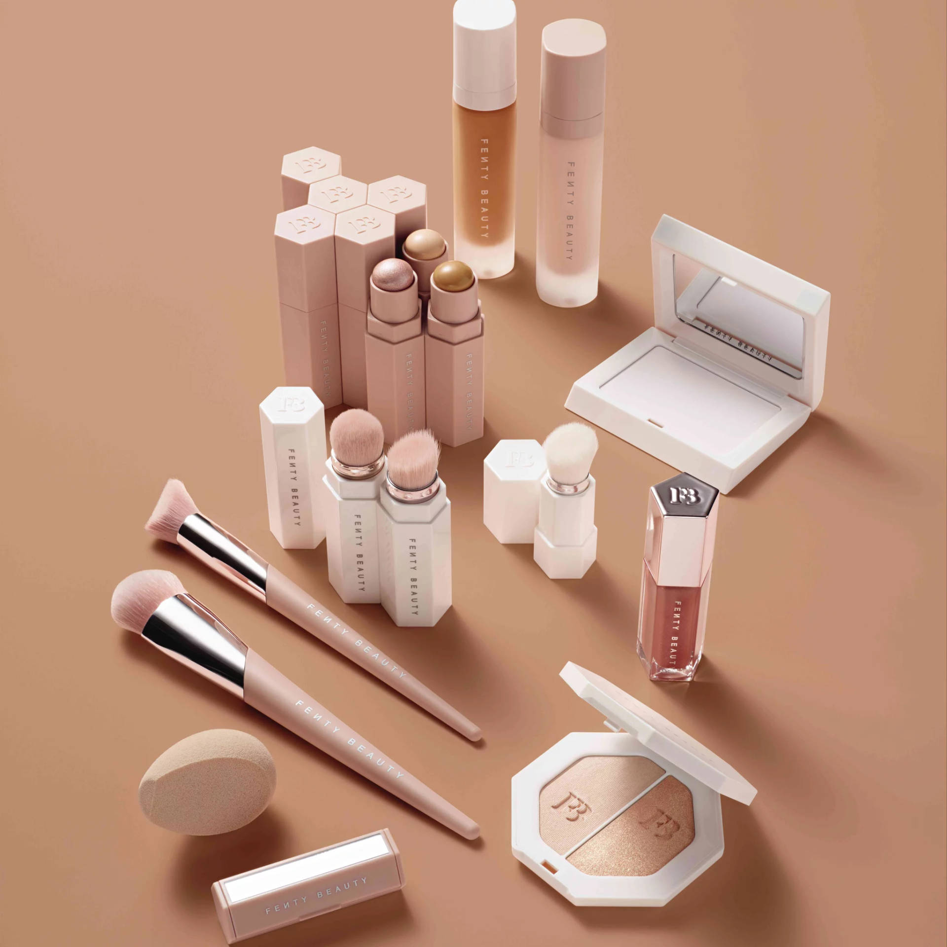 Fenty Beauty化妝品系列，附有刷具和粉餅，背景為米色