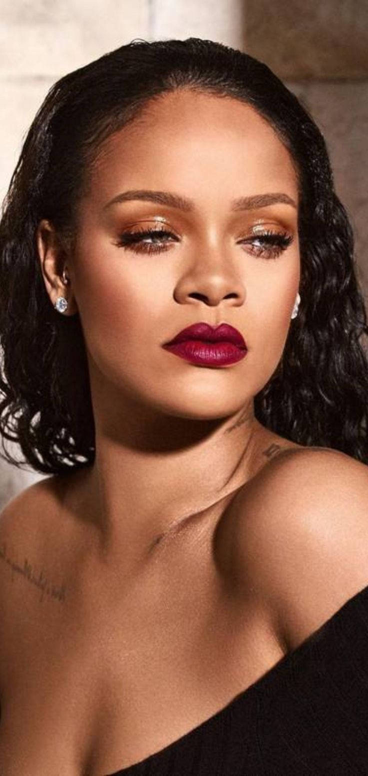 Rihanna 身穿黑色露肩上衣，擁有鮮豔紅唇和閃爍雙眼。