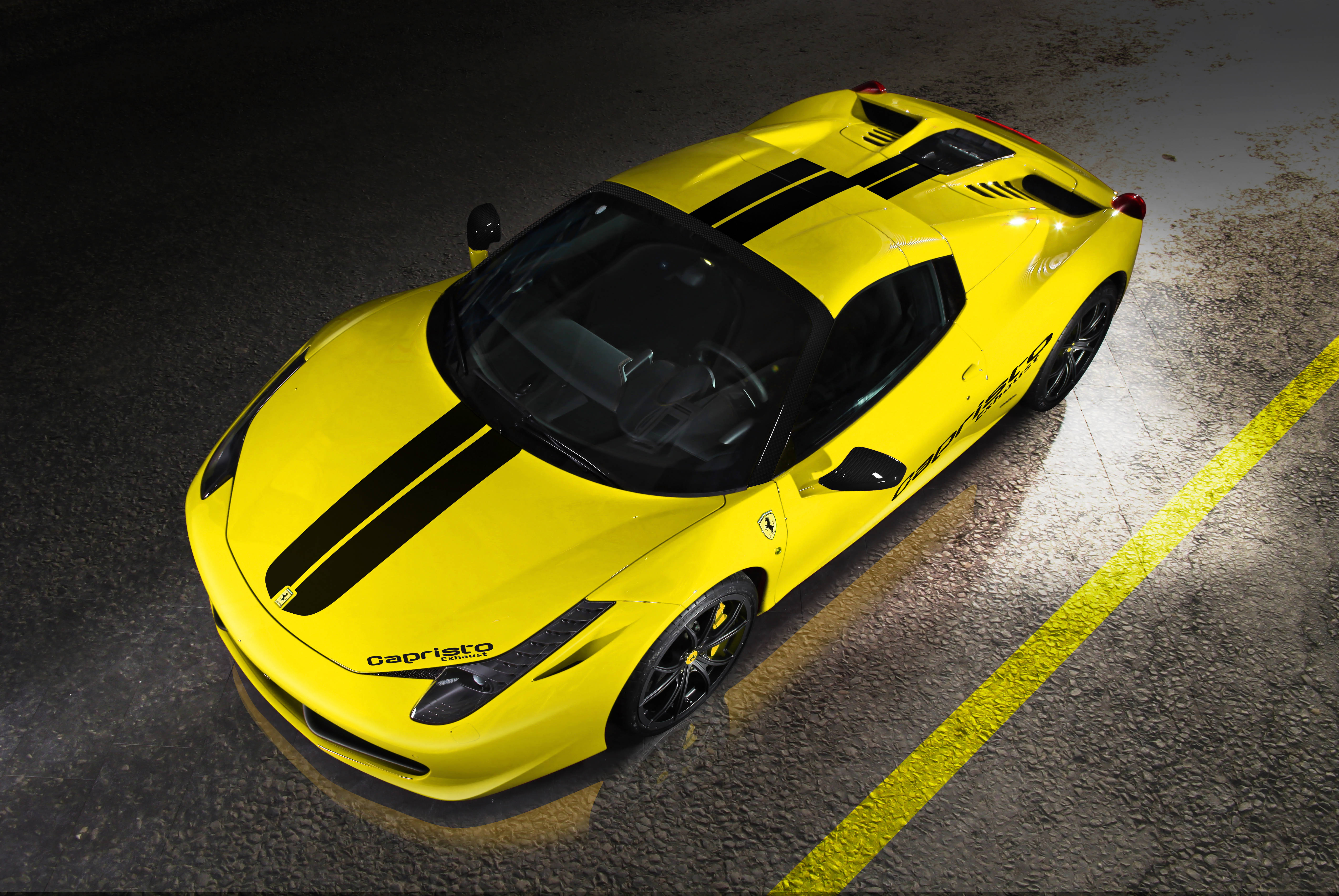 「Ferrari 458 Spider是動態中的藝術與力量」 壁紙 — 一輛鮮黃色的法拉利458 Spider帶有黑色賽車條紋，在濕瀝青賽道上於聚光燈下閃閃發光。