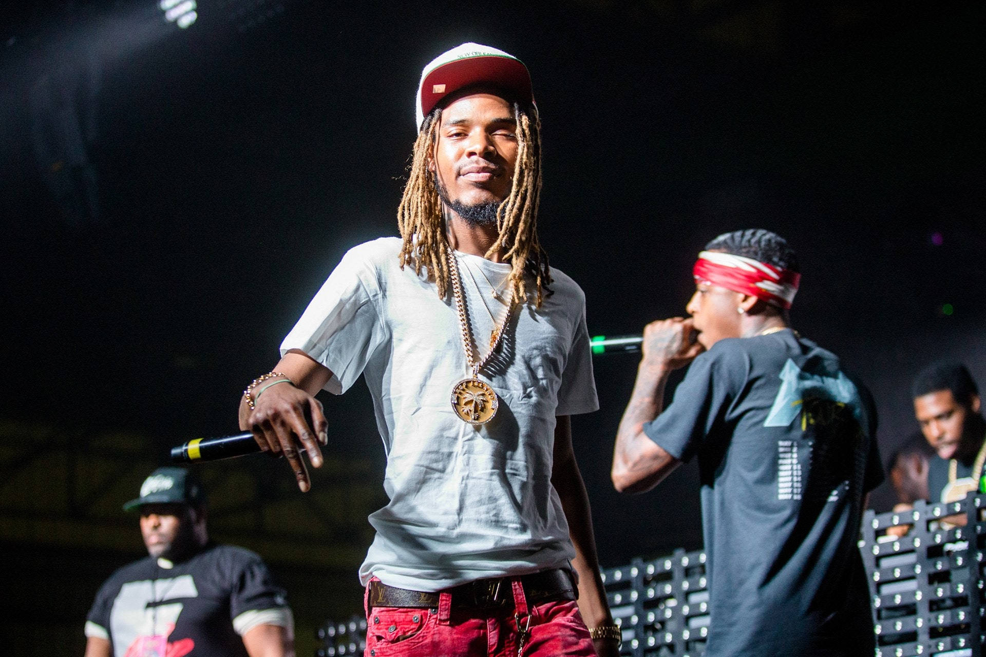 Fetty Wap 舞台演出 壁紙 — 一位梳著辮子頭、戴紅色帽子的說唱歌手在明亮的聚光燈下與伴唱一起在舞台上表演。