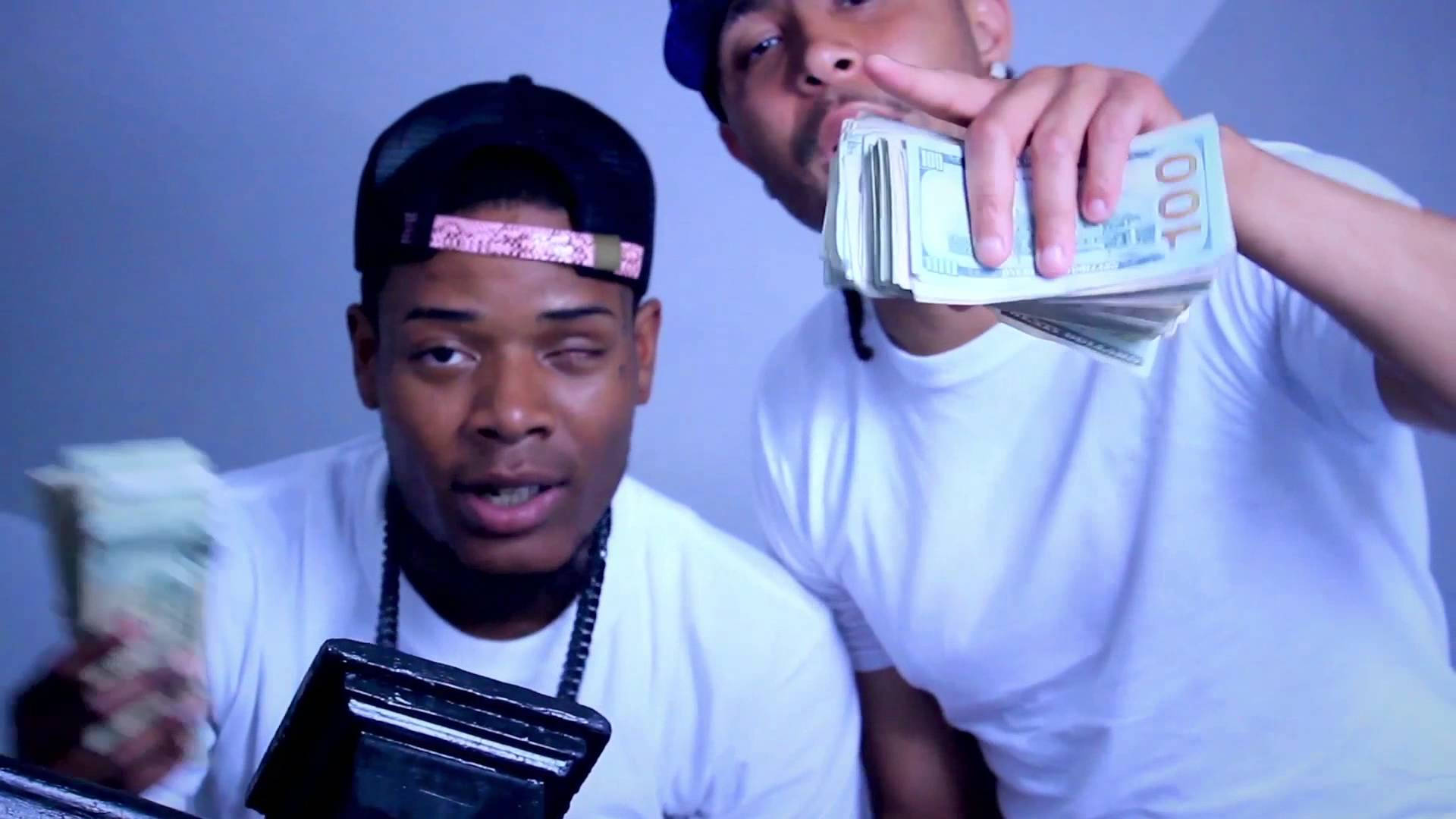 Fetty Wap L.A.X 音樂錄影帶 壁紙 — 兩名身穿白色T恤和帽子的男子，在純藍色牆壁前，手持一疊疊百元美鈔，表情強烈。