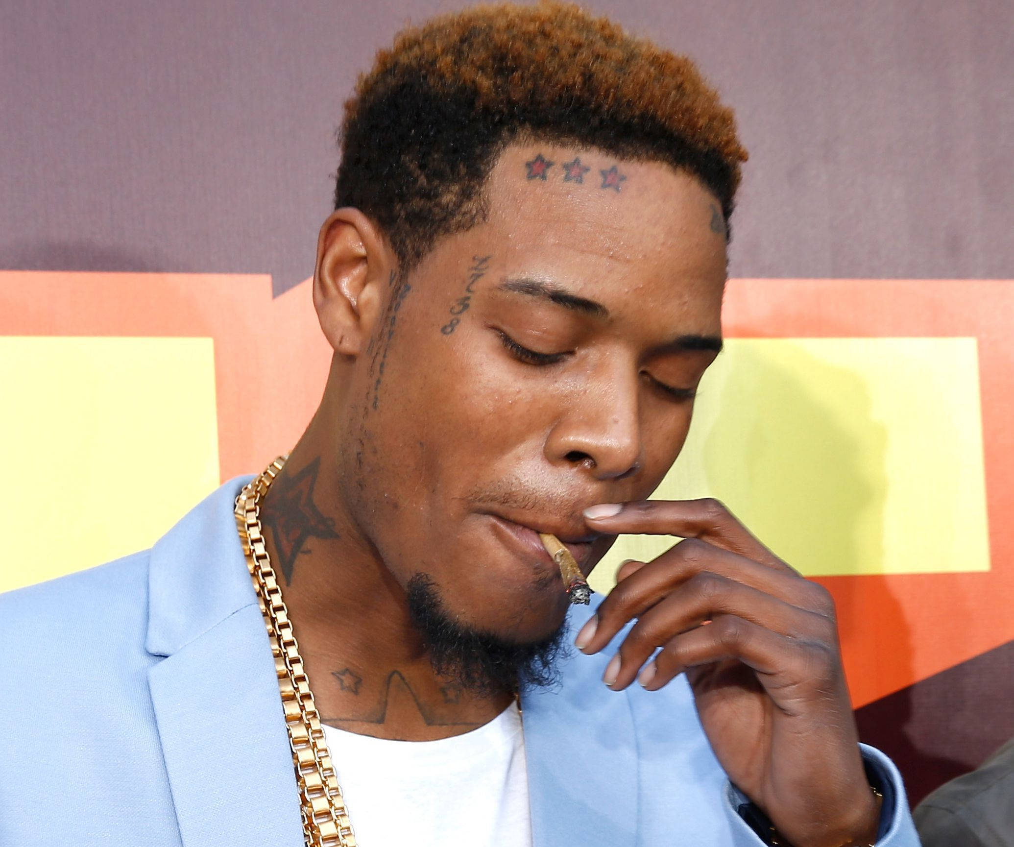 Fetty Wap 吸煙 壁紙 — 一名額頭上有星星紋身的男子，身穿淺藍色西裝外套和金色鏈條，正在吸煙。