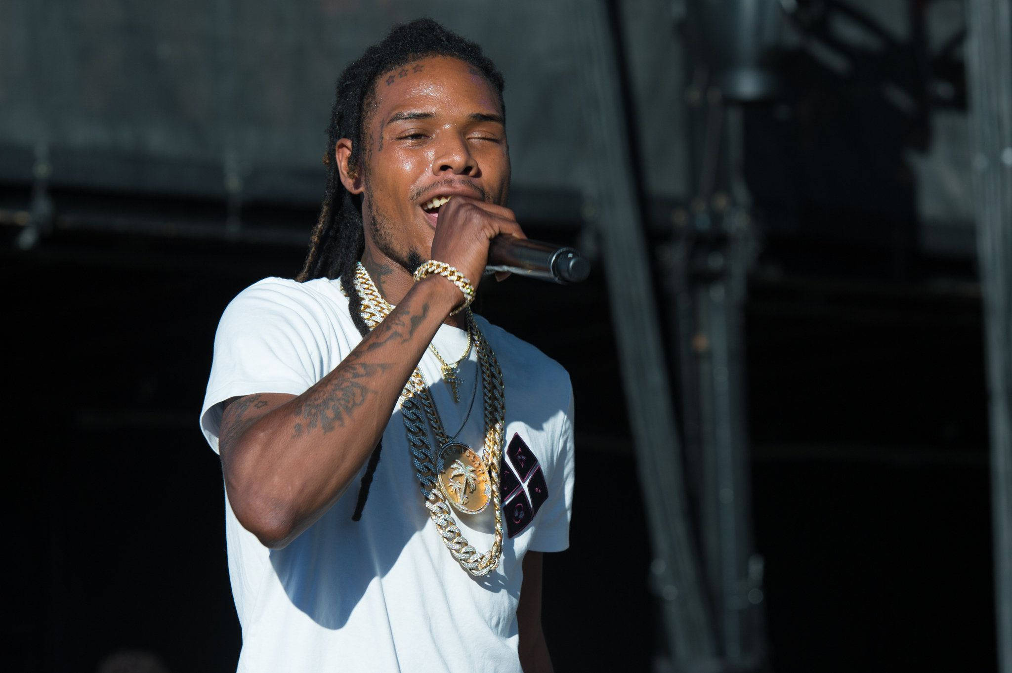 Fetty Wap 唱嘻哈 壁紙 — 一位男性饒舌歌手，梳著辮子頭，戴著金鏈，在明亮的舞台燈光下對著麥克風熱情表演。