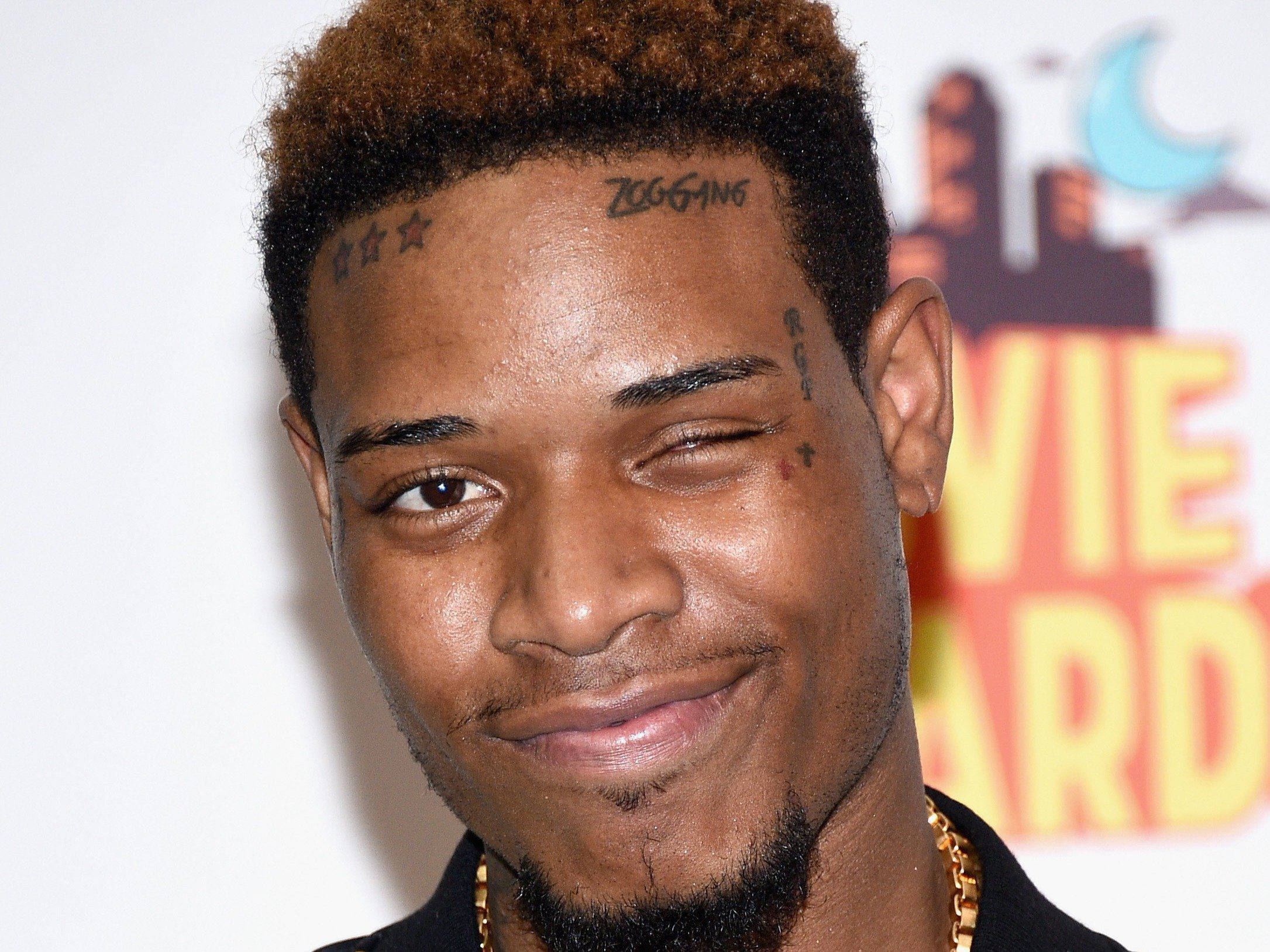 Fetty Wap 微笑特寫 壁紙 — 一個微笑男子的特寫肖像，額頭和頸部有紋身，戴著金鏈。