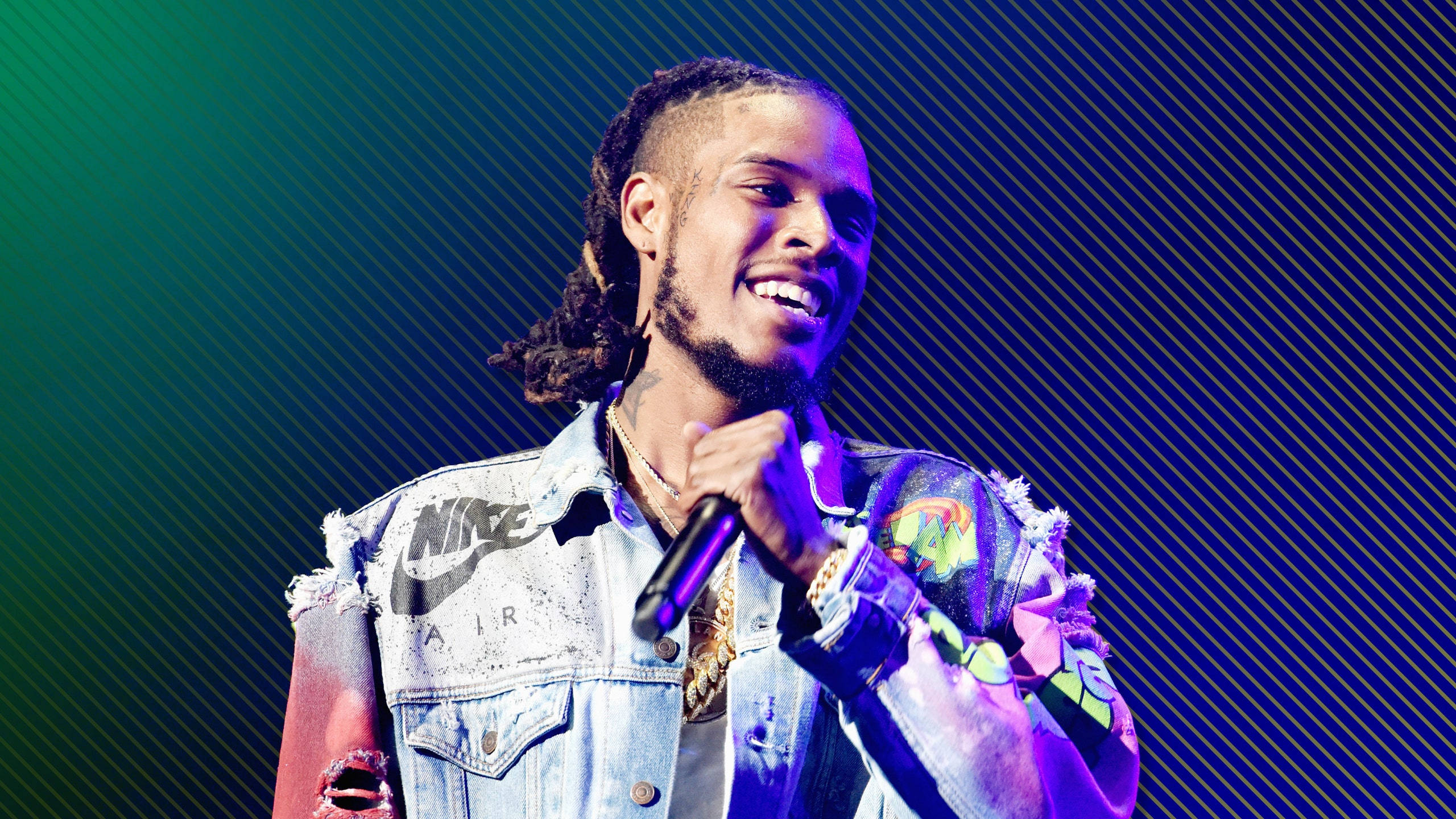 Fetty Wap 梯度背景 壁紙 — 一位微笑的男歌手留著辮子，在充滿活力的藍色和綠色對角燈光下拿著麥克風在舞台上表演。