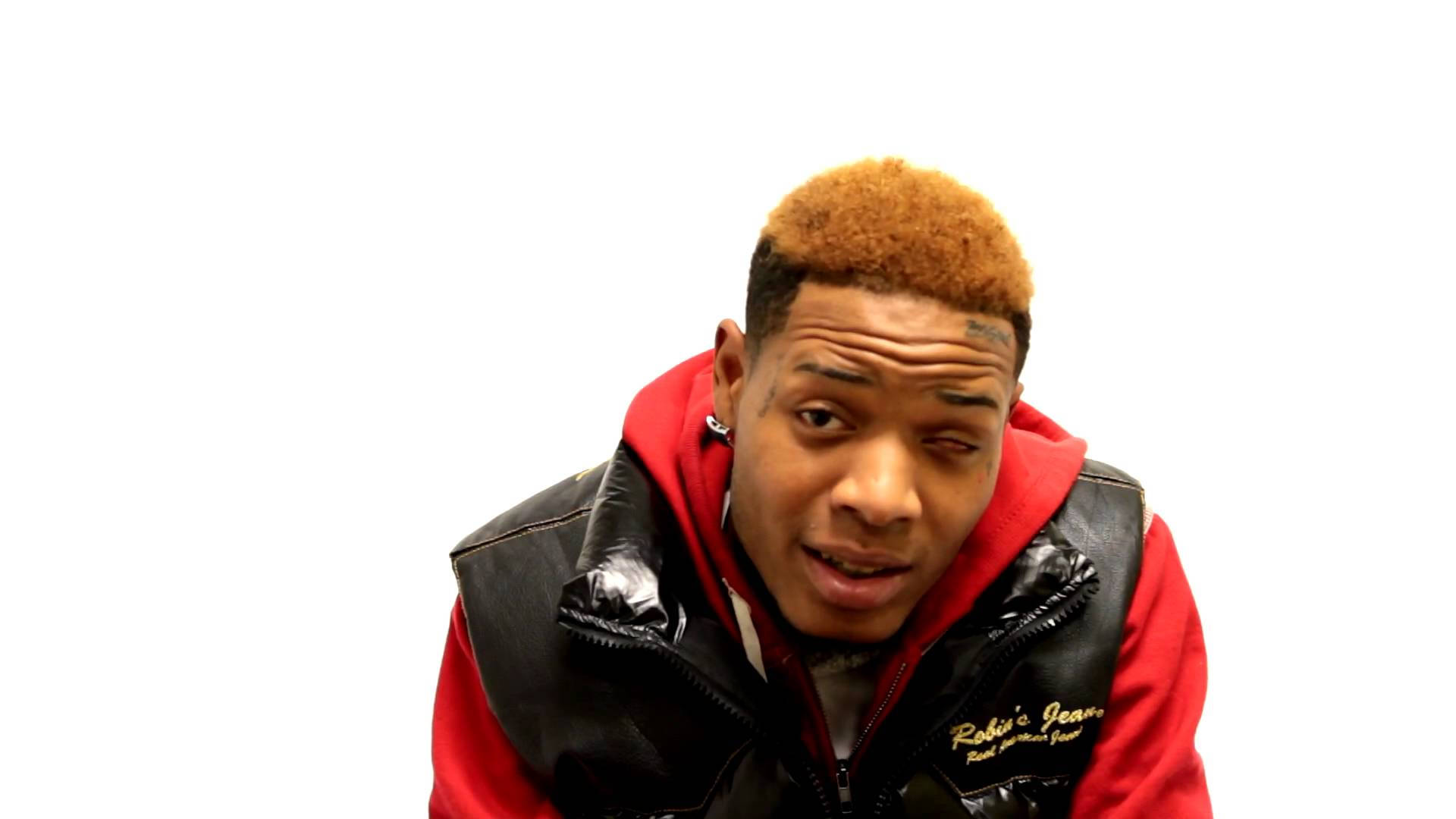 Fetty Wap 穿白衣 壁紙 — 一位橙髮青年身穿黑色背心內搭紅色連帽衫，在純白背景下凝視前方。