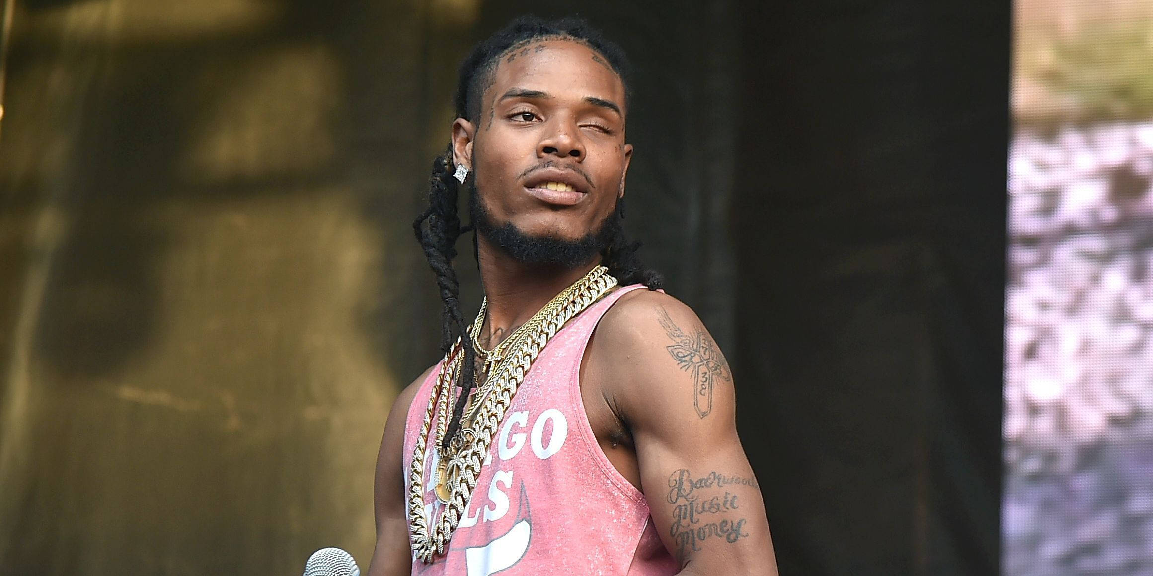 Fetty Wap舞台聚焦攝影 壁紙 — 一位男饒舌歌手，梳著辮子頭，戴著金鏈，身穿粉紅色背心在舞台上表演。