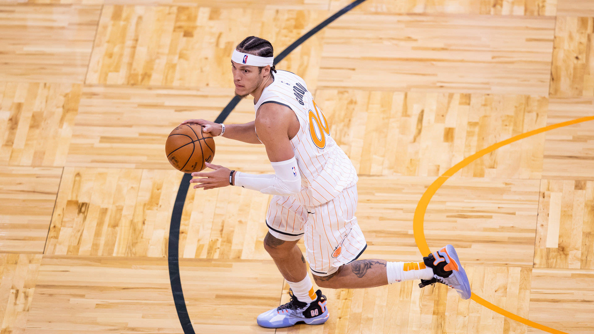 FIBA世界盃MVP亞倫·戈登 壁紙 — 一名身穿白色和橙色球衣的籃球運動員在明亮的場館燈光下，在拋光木地板上低運球。