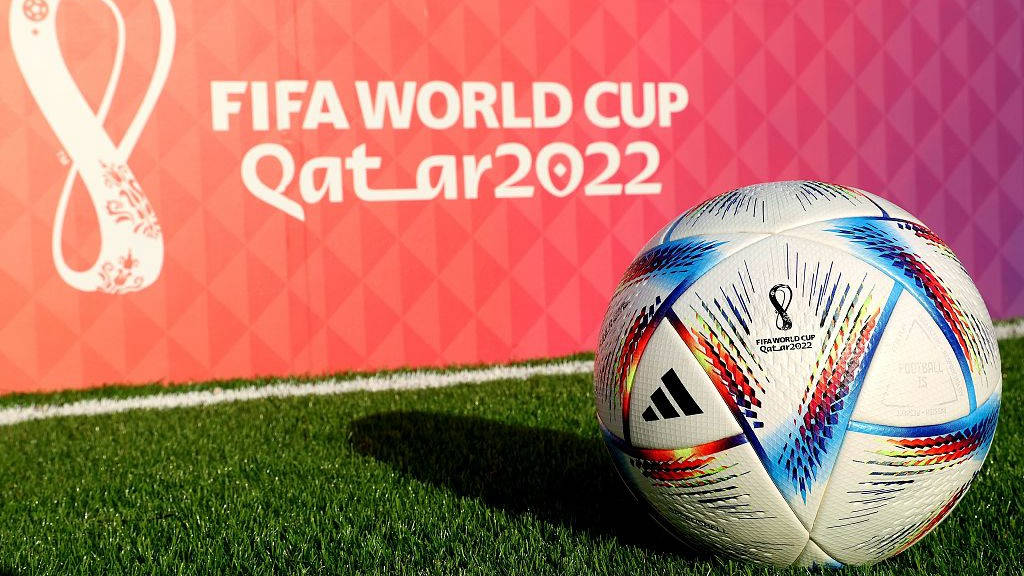 卡塔爾國家足球隊FIFA比賽用球 壁紙 — 一個充滿活力的FIFA世界盃卡塔爾2022足球放在綠色草地上，背景是粉紅色圖案和活動品牌標誌。