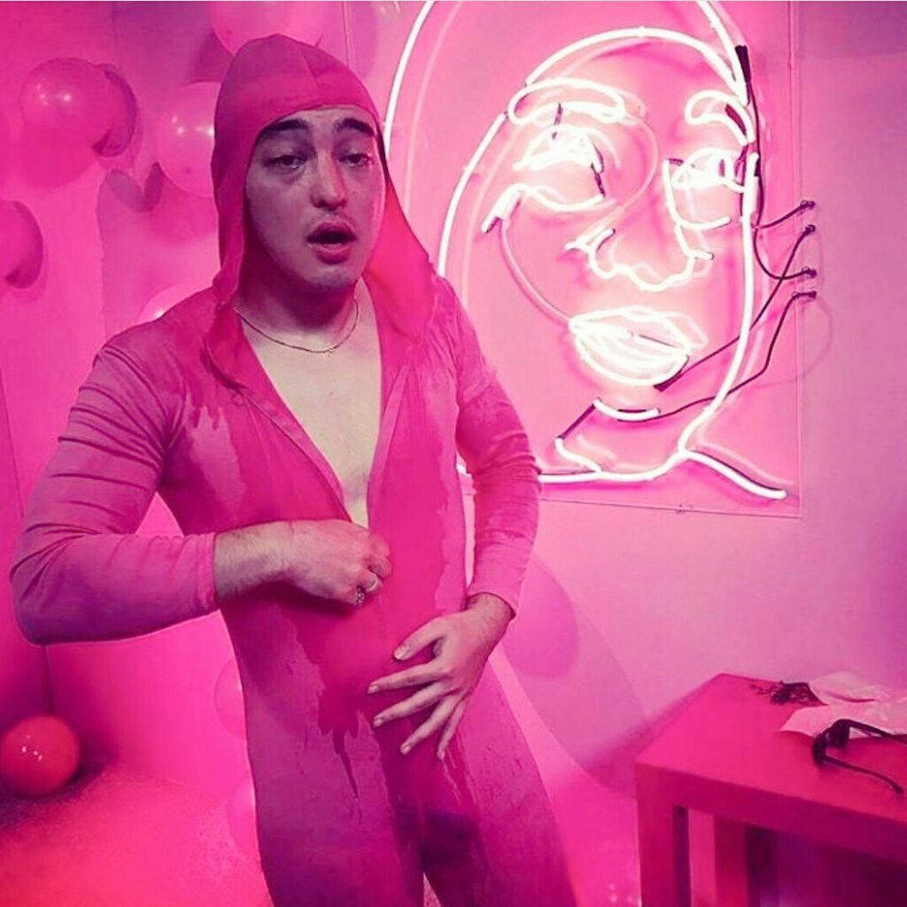 在霓虹粉紅色的房間裡，穿著粉紅色衣服的人與發光的臉部藝術品。