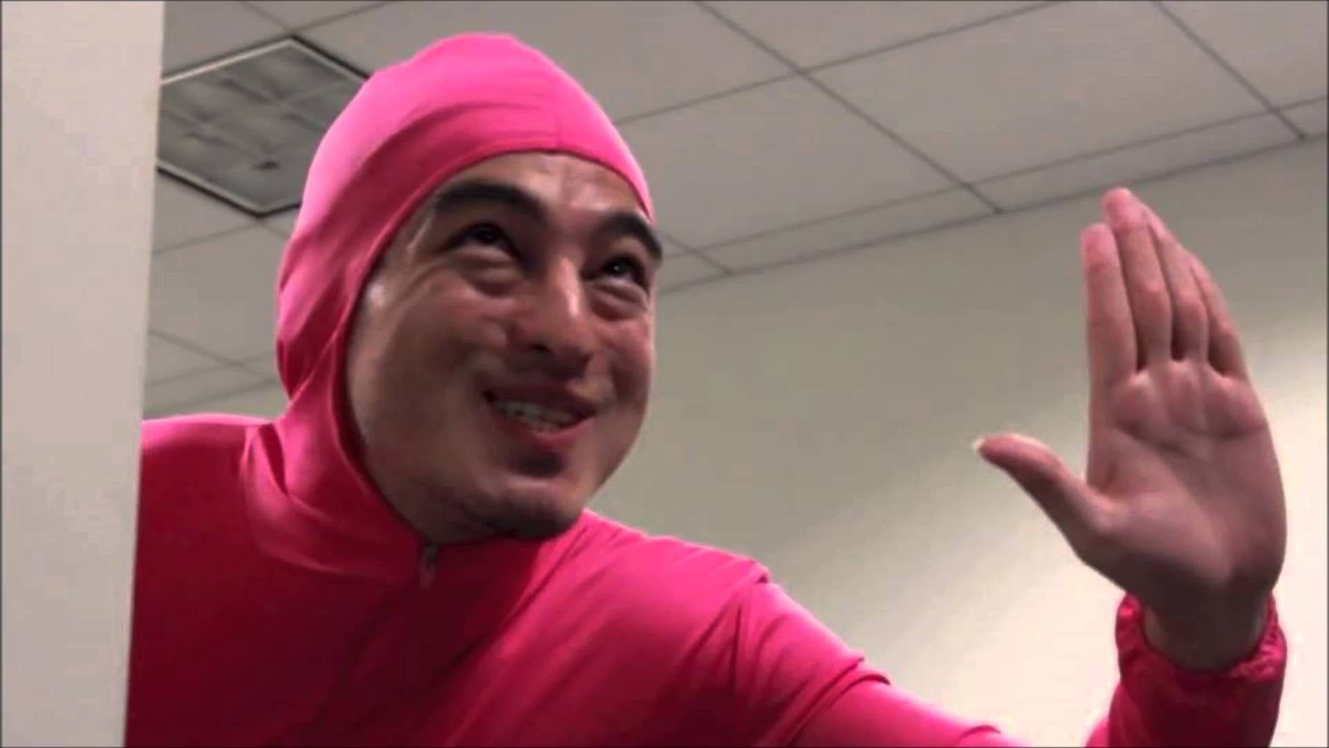 身穿粉紅色套裝的男子在室內微笑揮手。