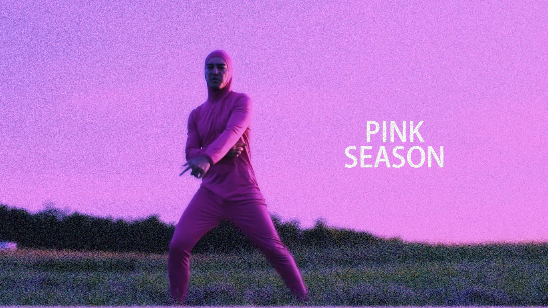 穿粉紅色套裝的人在暮色田野中持刀，文字 pink season。
