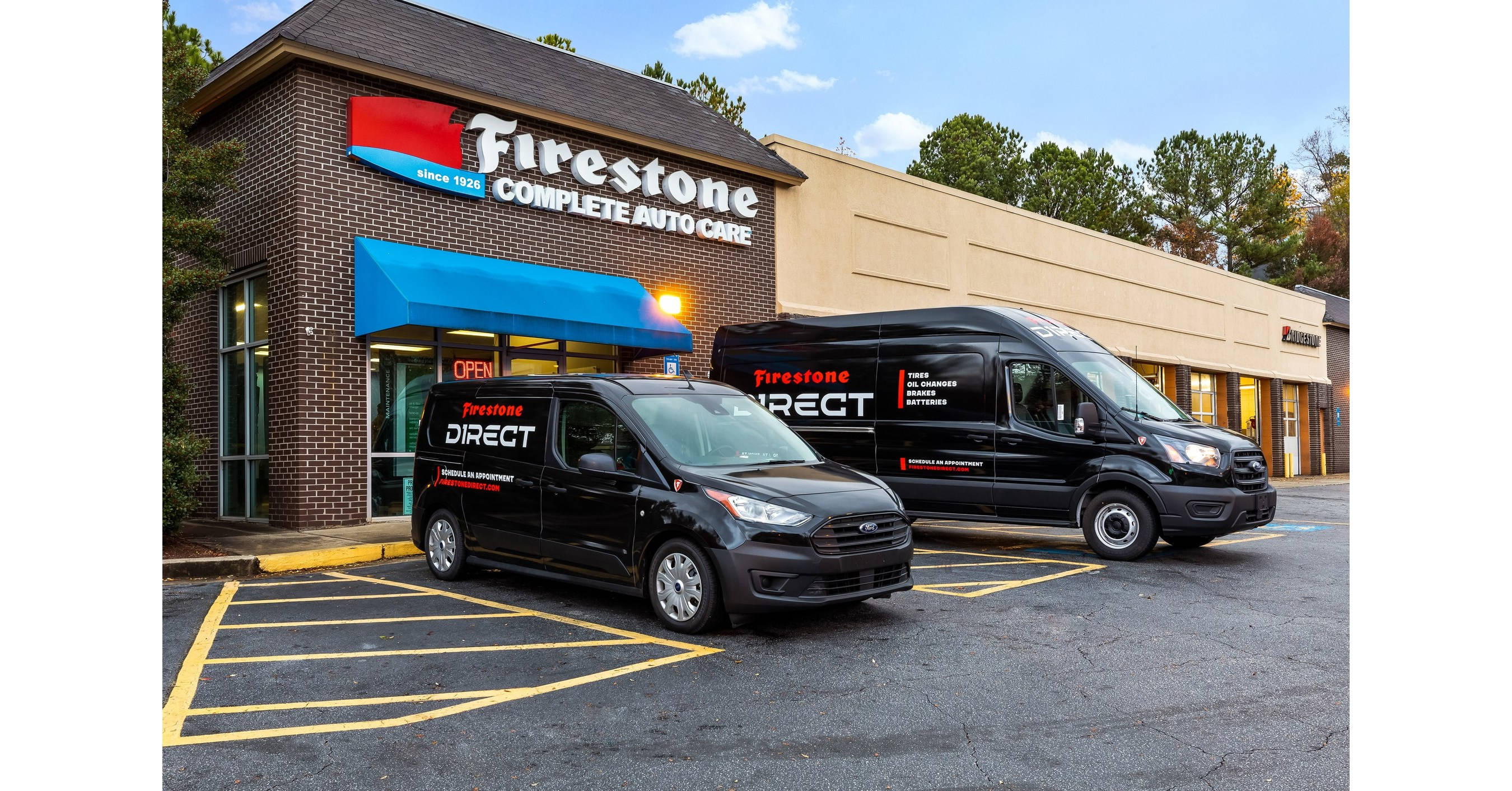Firestone 輪胎店前停泊兩輛汽車 壁紙 — 兩輛黑色Firestone Direct貨車停泊在磚砌汽車維修店前，天空清澈湛藍。
