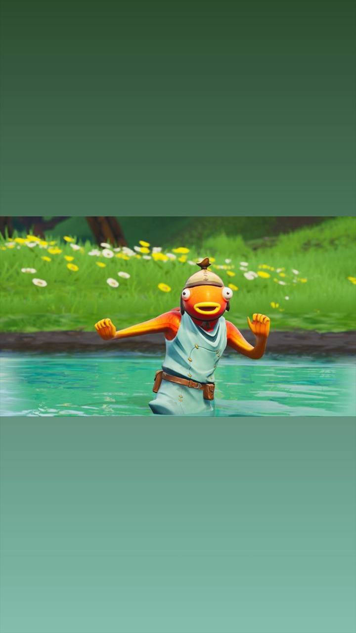 Fishstick Fortnite 稀有皮膚 壁紙 — 一個卡通橙色魚角色穿著淺藍色衣服，站在清澈的水中，水深及腰，背景是長滿黃色和白色花朵的草地。